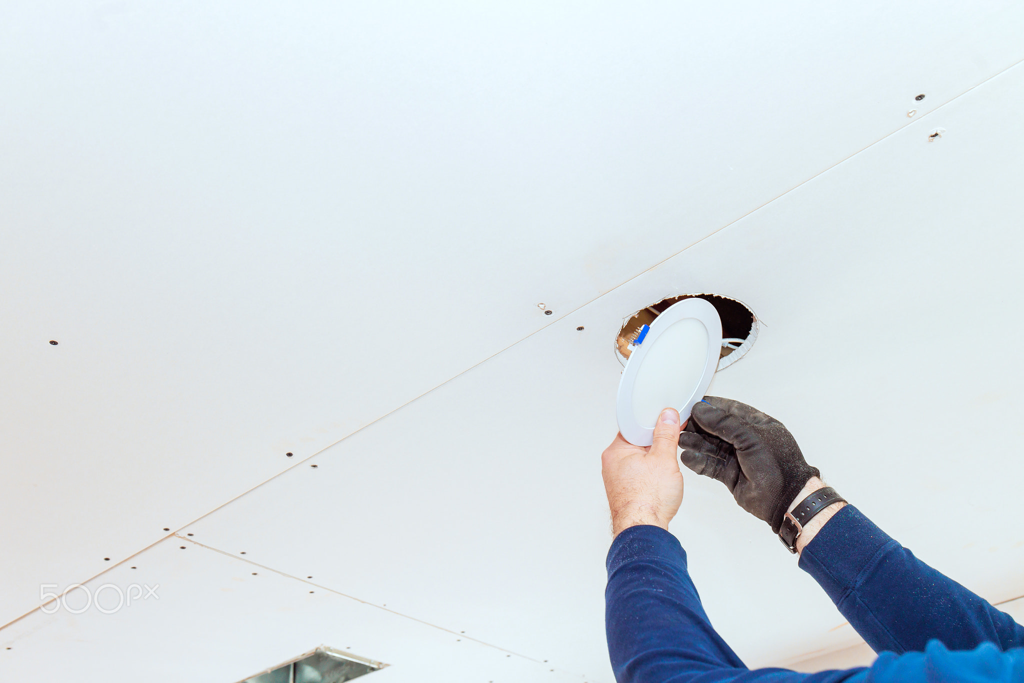 Professional electrician installs recessed lighting fixture in a