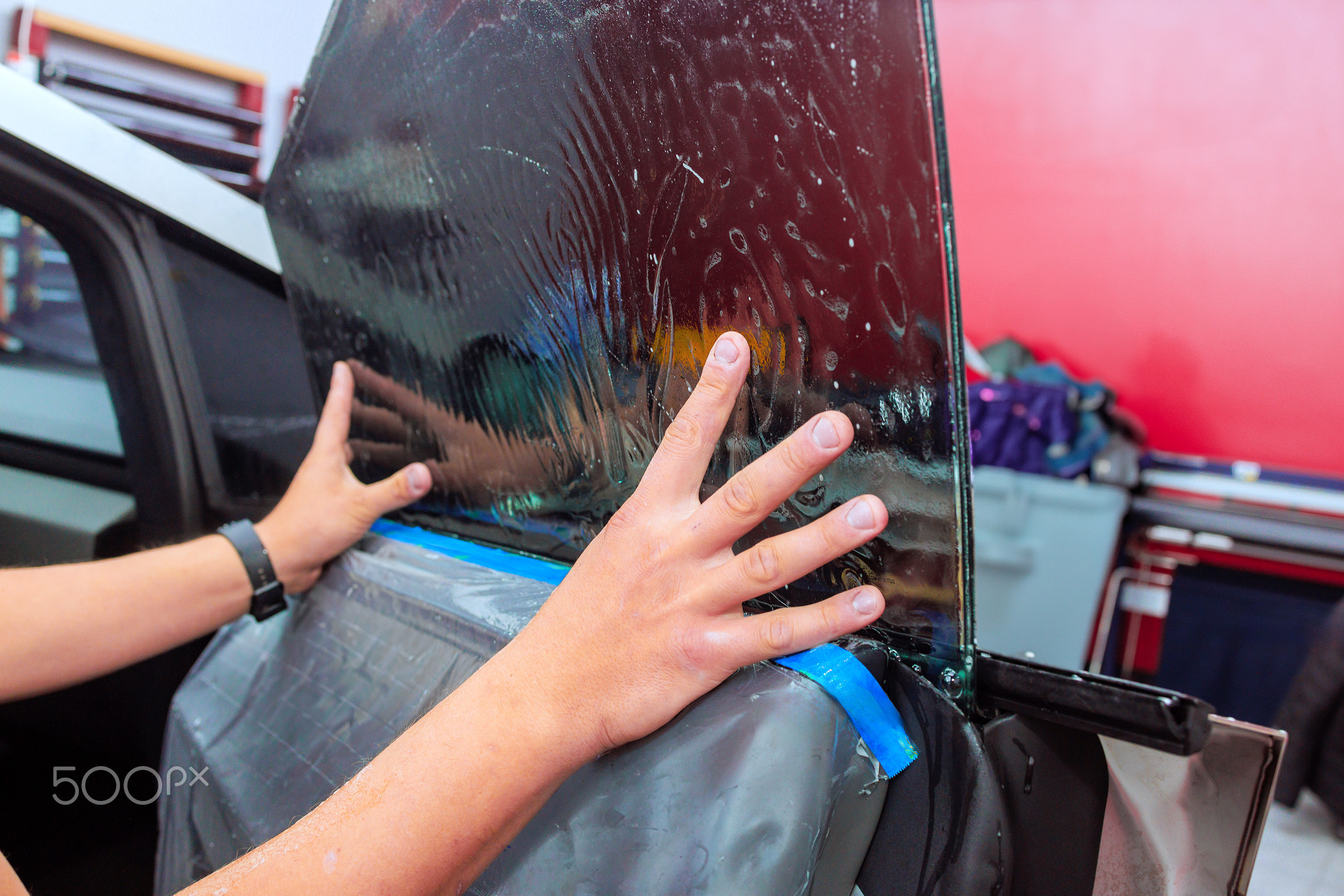 Professional installation of window tint on a car door at an auto shop
