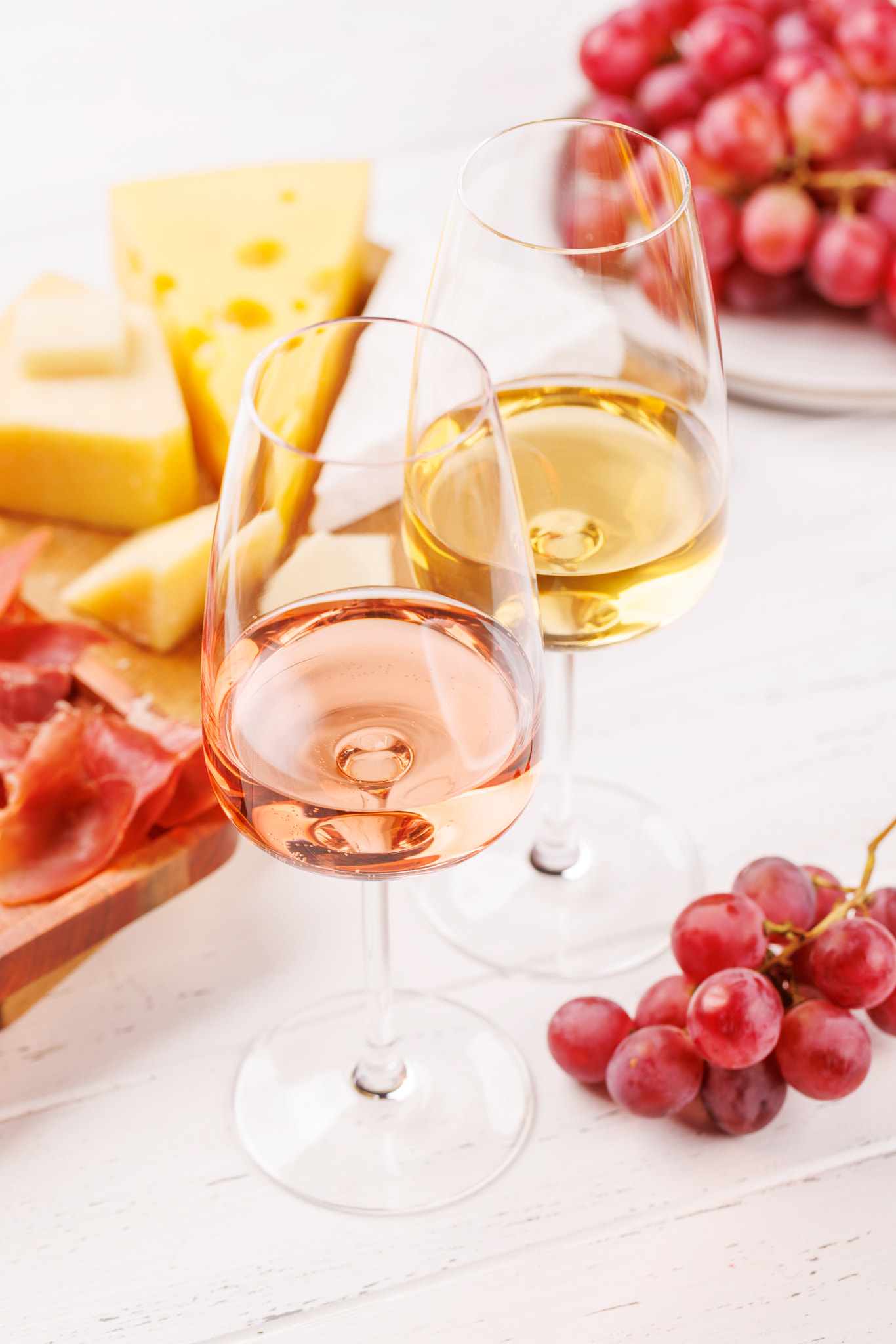 A delectable arrangement of various cheeses, fresh grapes, prosciutto and wine