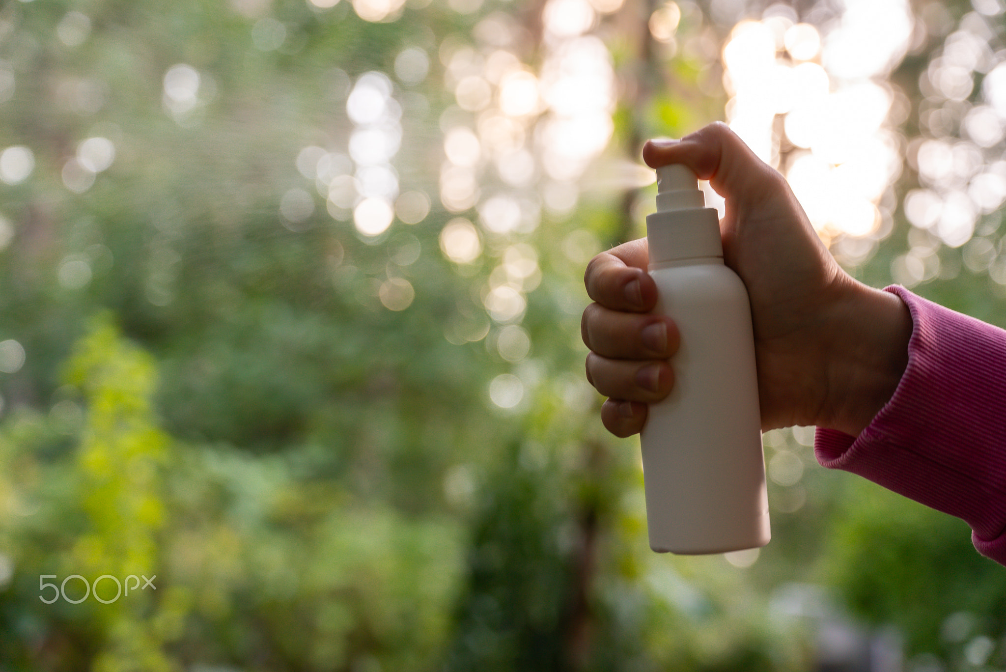 Person spraying insect repellent at her hand outdoors during summer