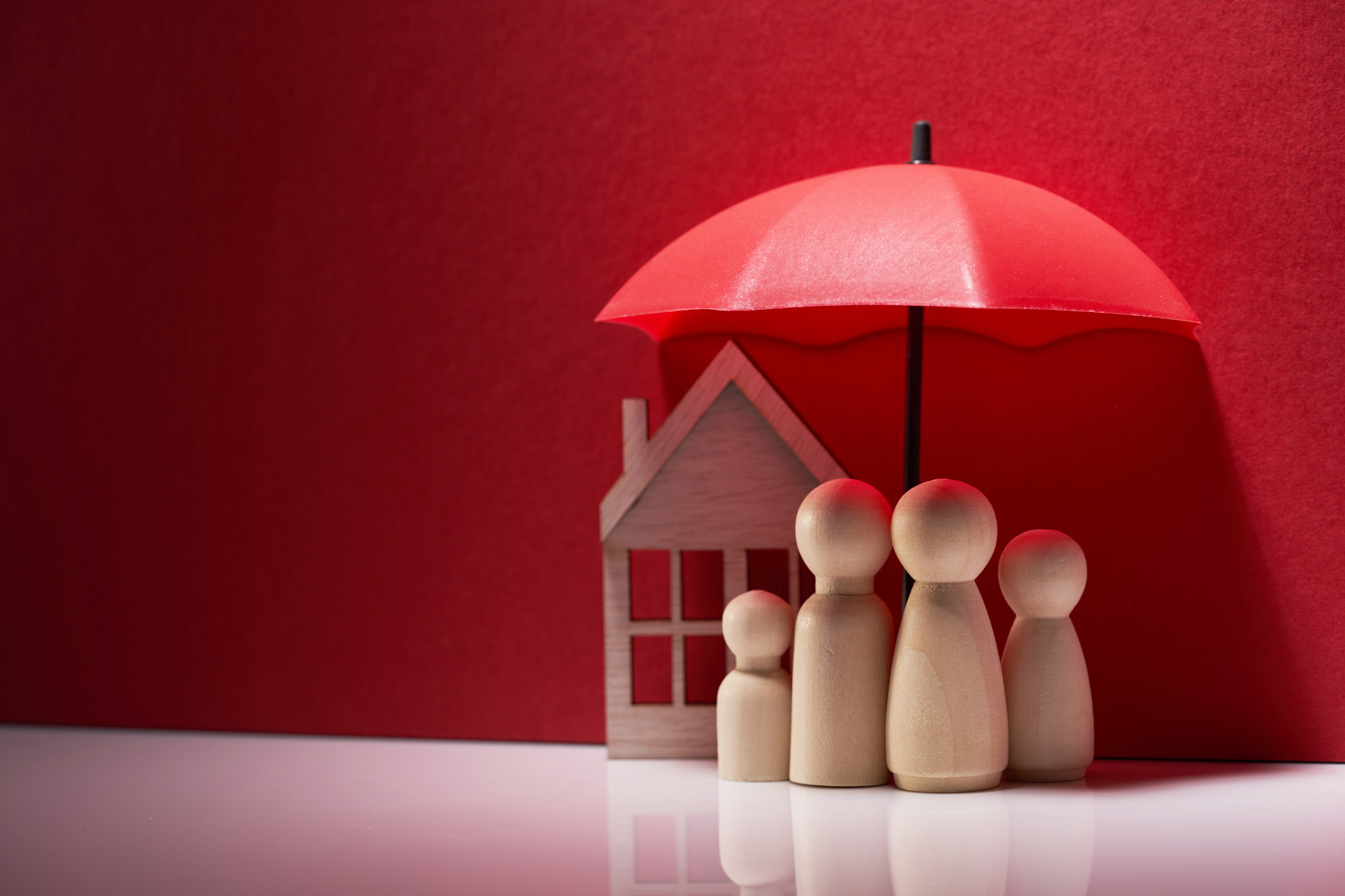 Family people wood figures holding umbrella with model house as background 