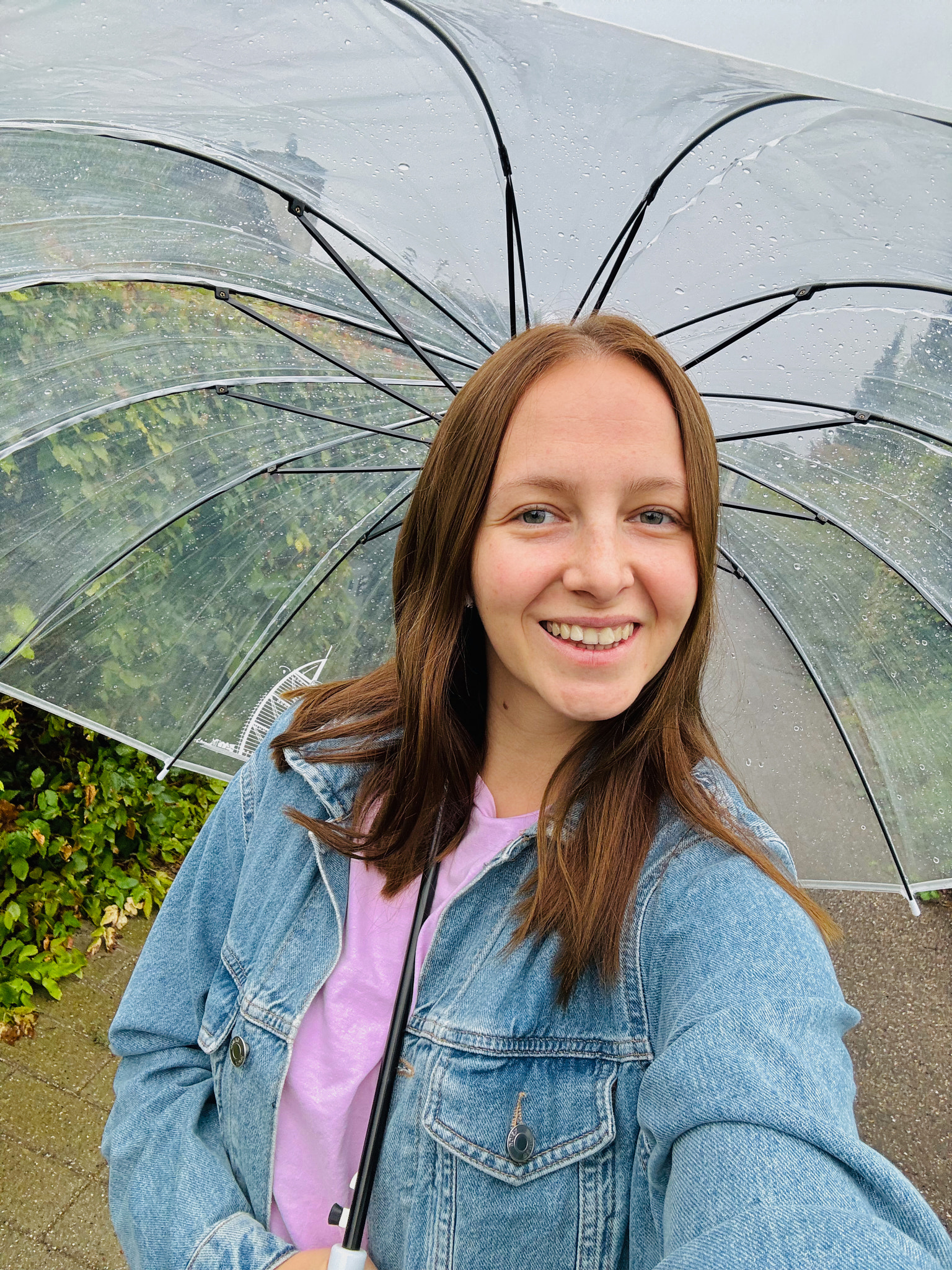 Selfie portrait of smiling woman holding umbrella while standing against trees during rainy season