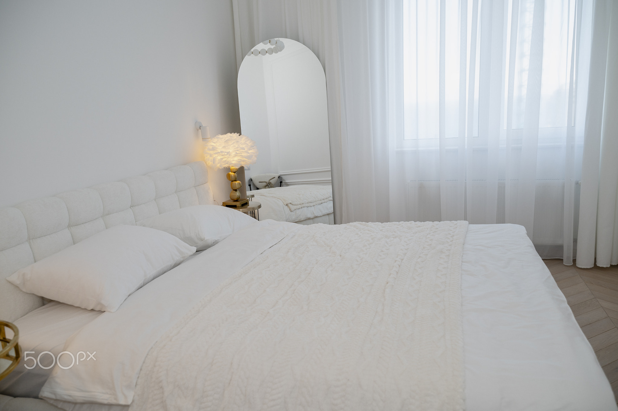 Interior of a bright bedroom, a bed with a white headboard, a white blanket and bed linen