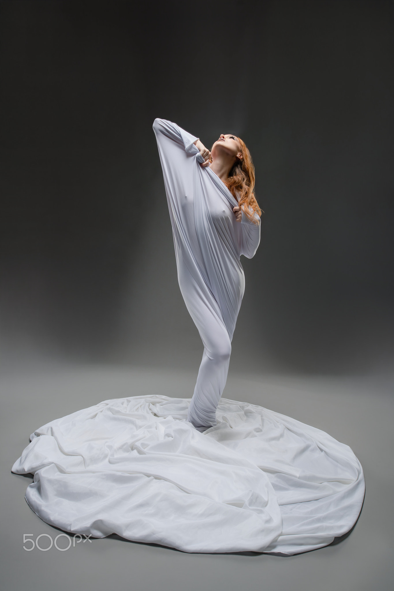 A dancer emerges gracefully from flowing white fabric in a studio setting