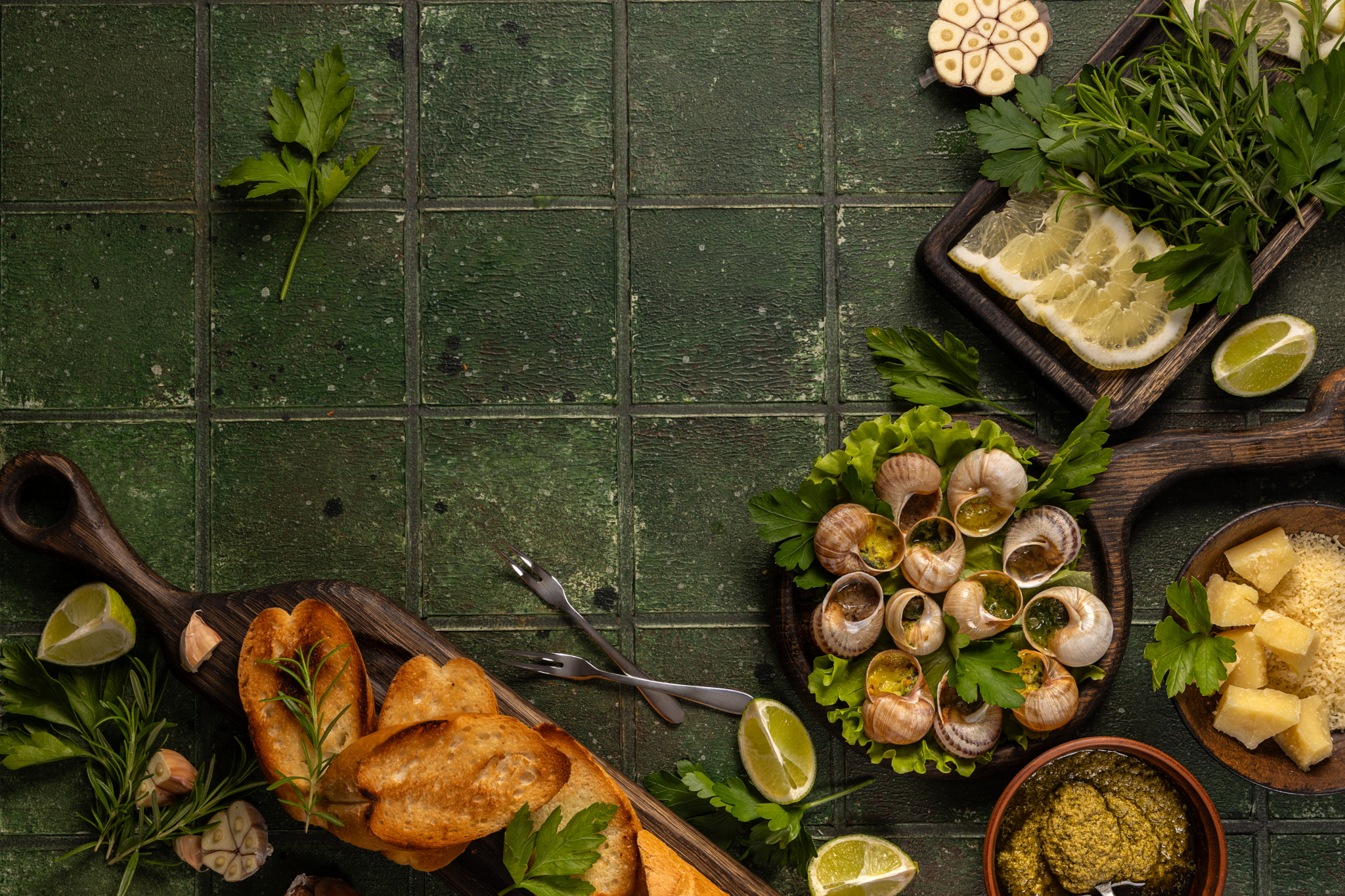 Snails with garlic butter, parsley, and toasted baguette slices on green tiles