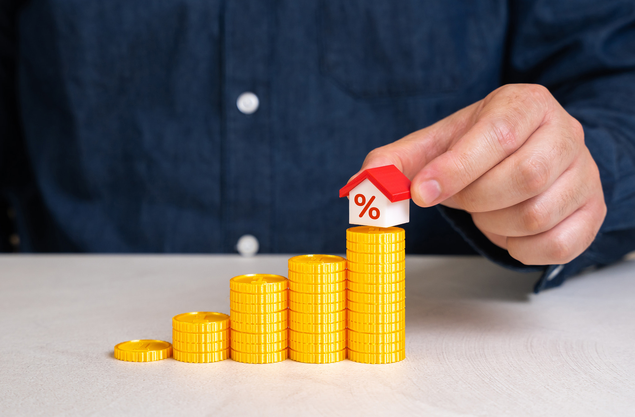 A man places a house on top of a staircase made of coins. Saving for a house. Down payment and openi