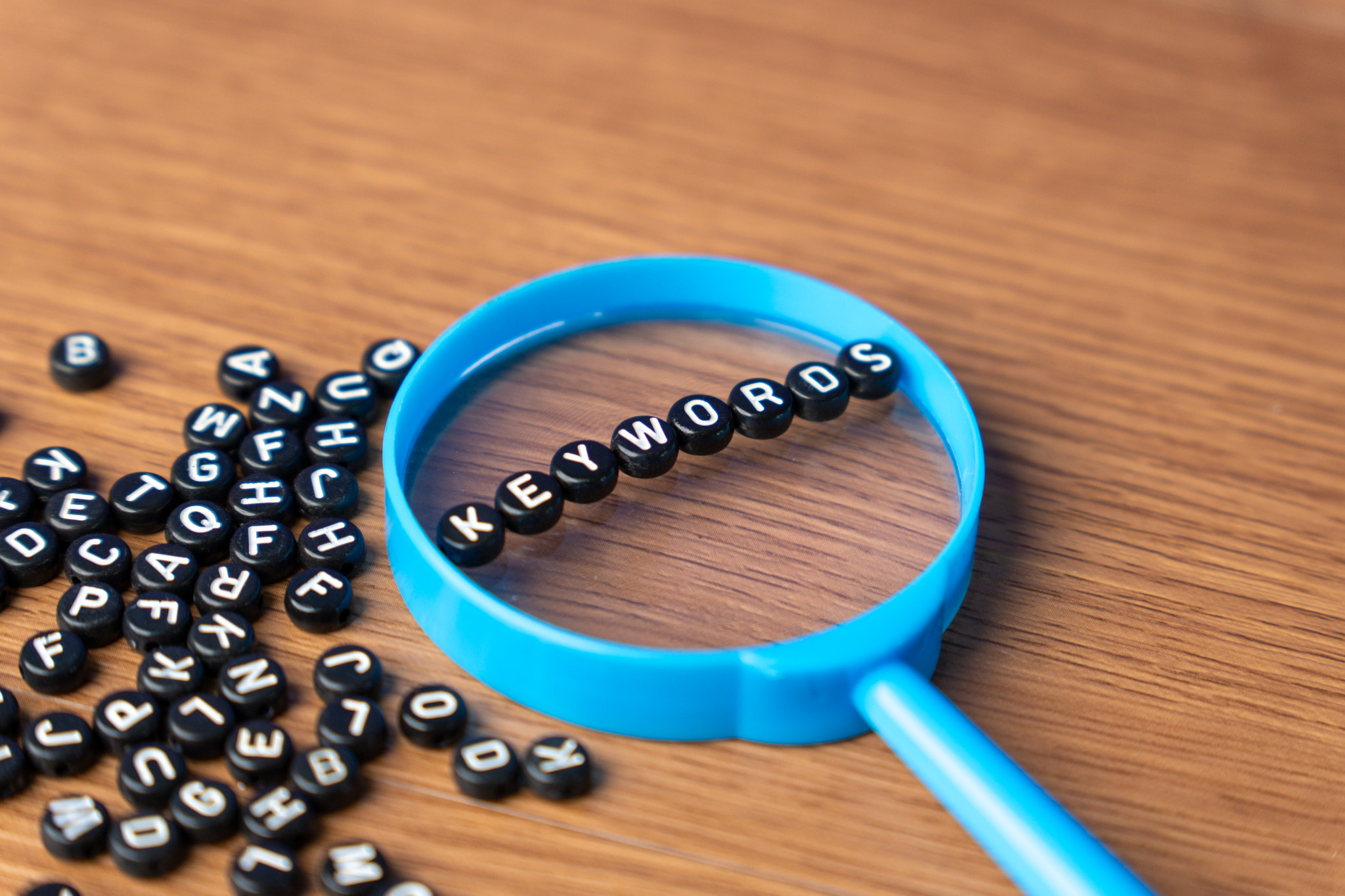 A blue magnifying glass with alphabet beads that spell out KEYWORDS.