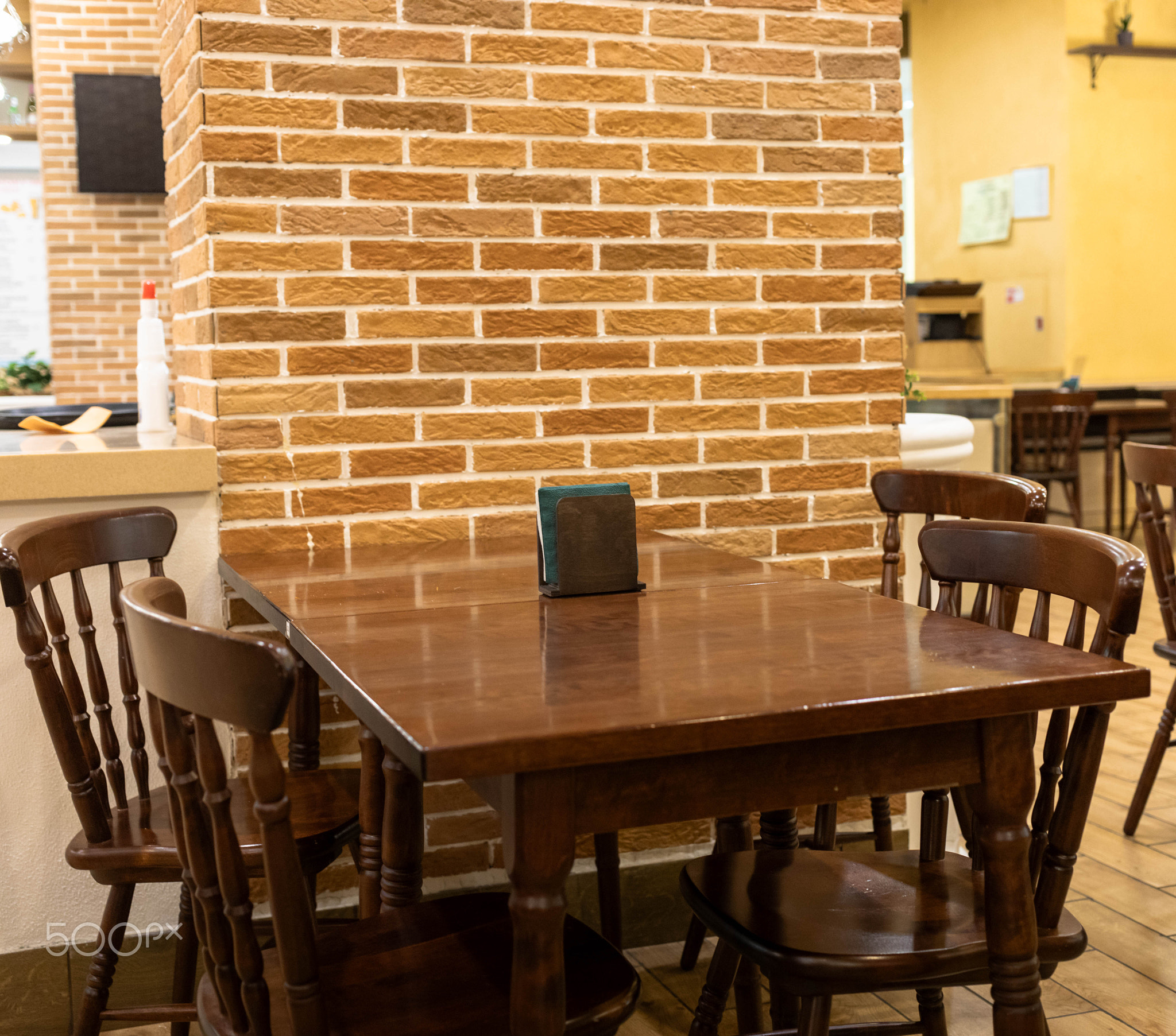 Wooden dining table with chairs in cozy restaurant interior featuring brick wall design