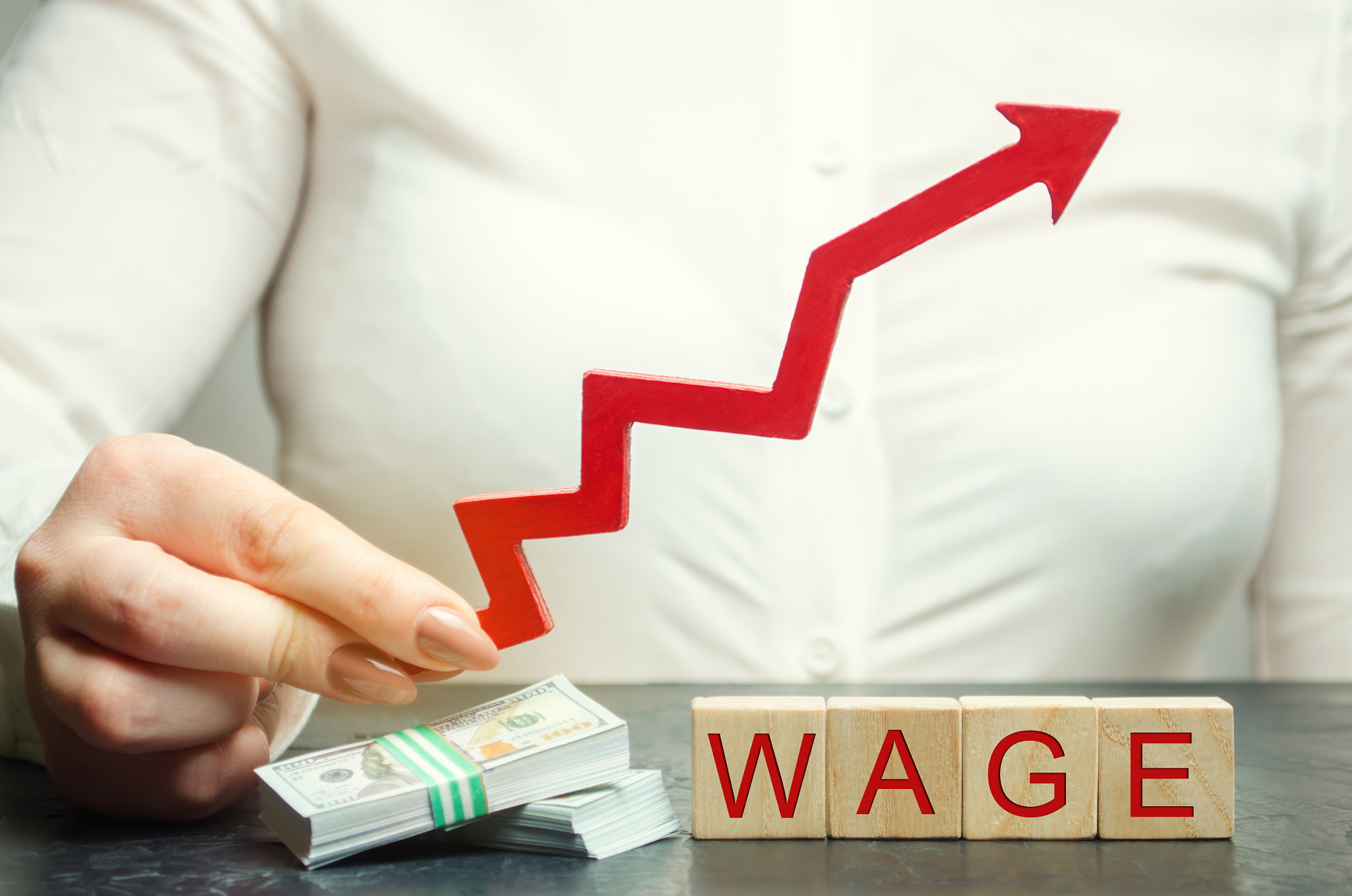 Female hand holds arrow up above word wage. Increase of salary, wage rates. Promotion, career growth