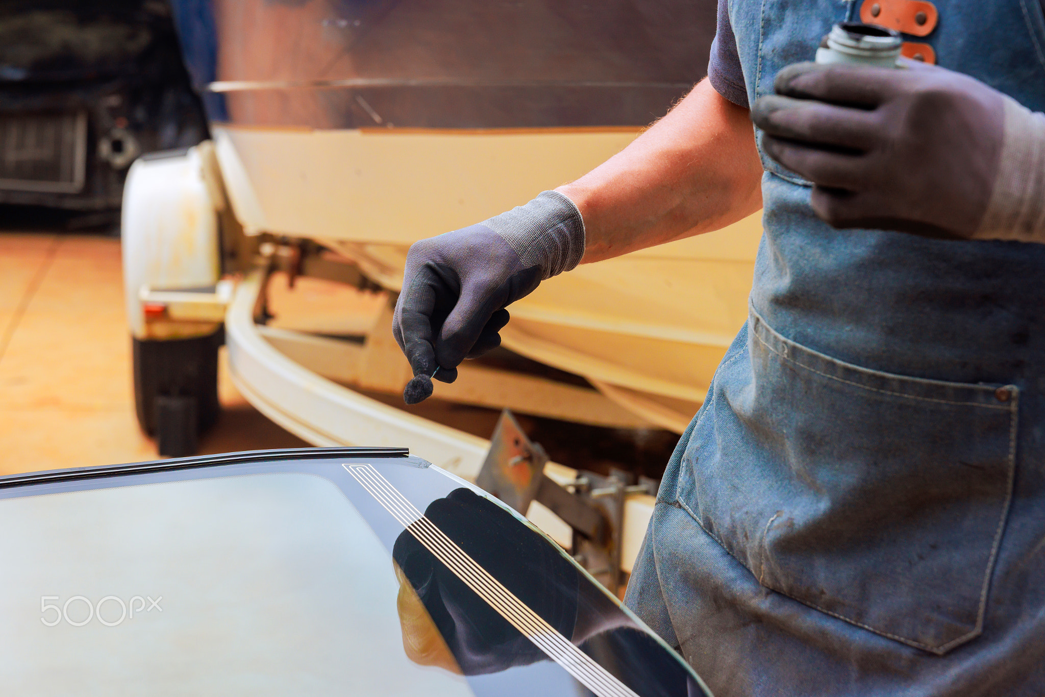 Car detailing process with worker applying sealant on vehicle in