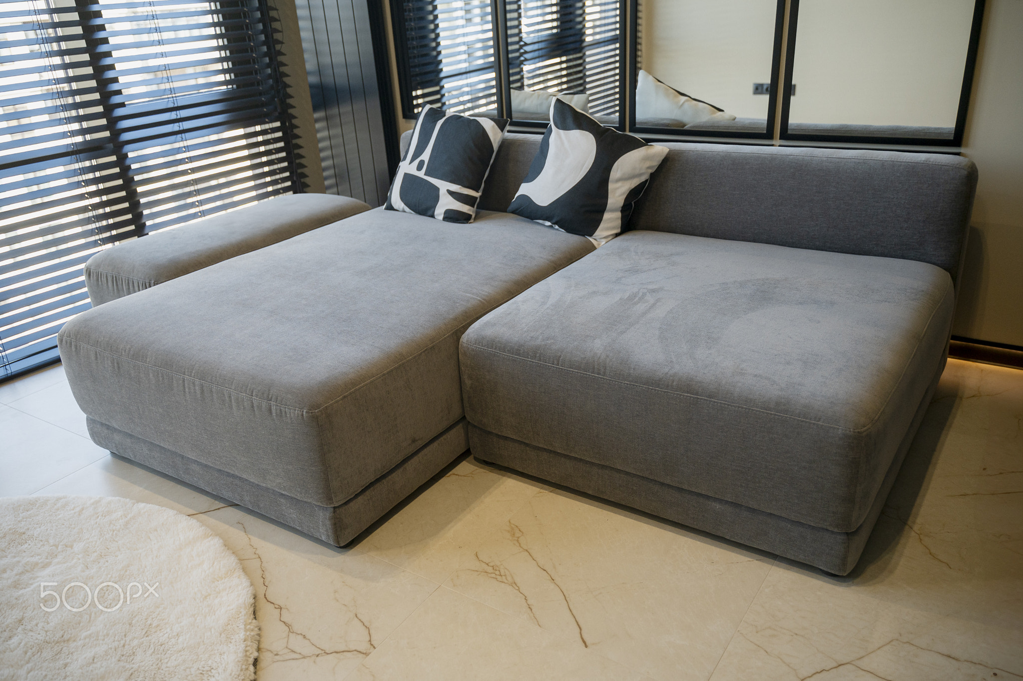 Ergonomic gray, velour sofa standing near a large window with wooden blinds with copy space