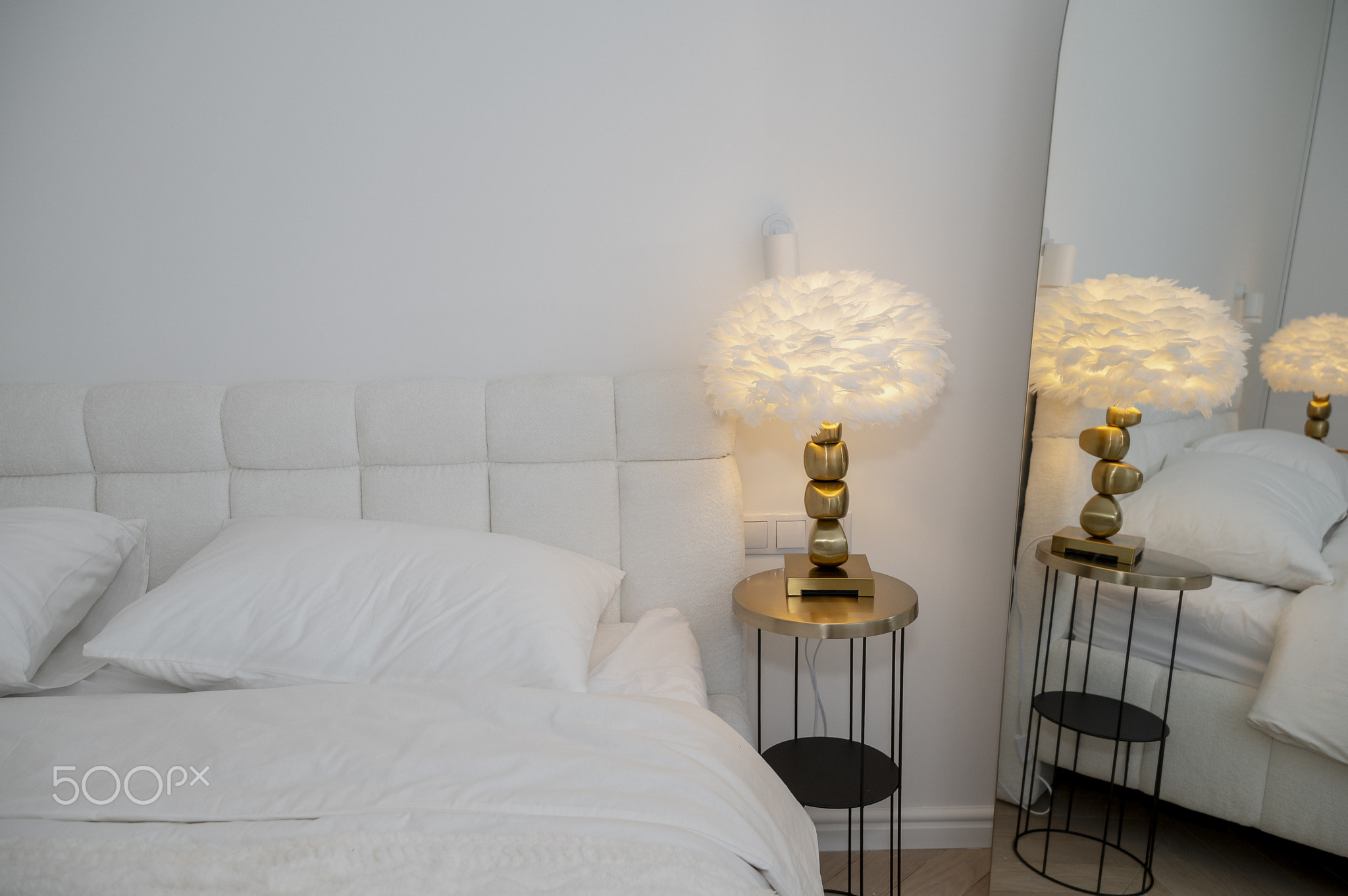 Bedroom interior with modern reading lamp on table next to double bed with pillow.