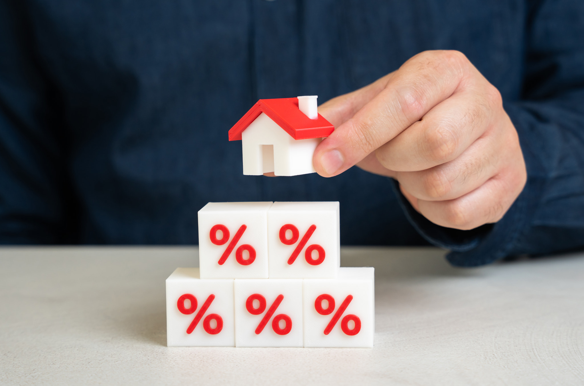 A man holds a house over a pyramid of interest. Cost burden of mortgage loans. Rising interest rates