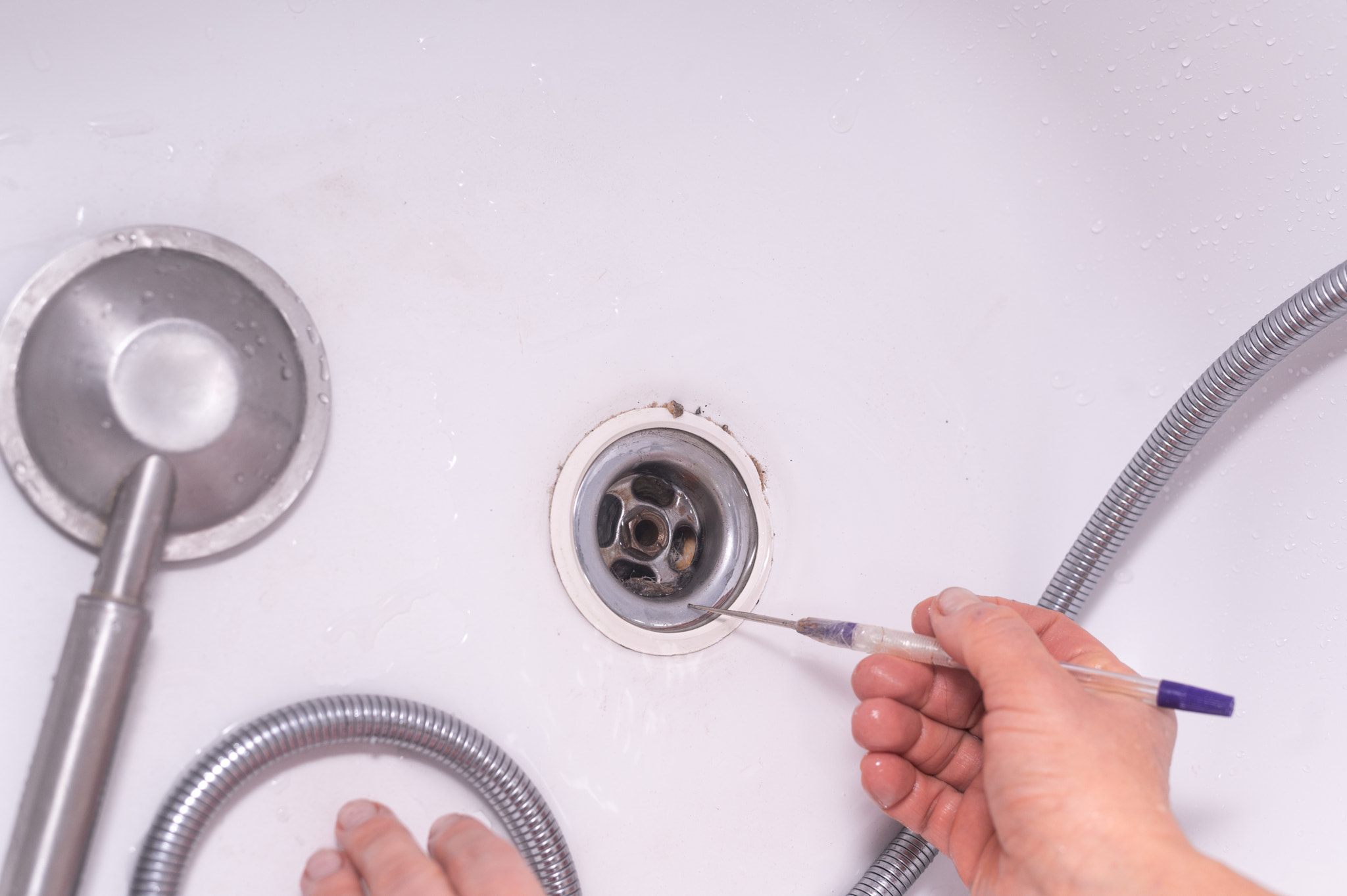 Bathroom maintenance in progress as person removes blockage from drain using tool. Manual removal of