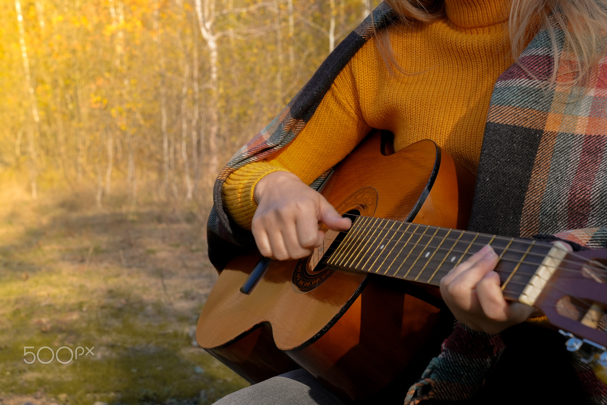 Close up of hands playing string guitar outdoors in autumn forest