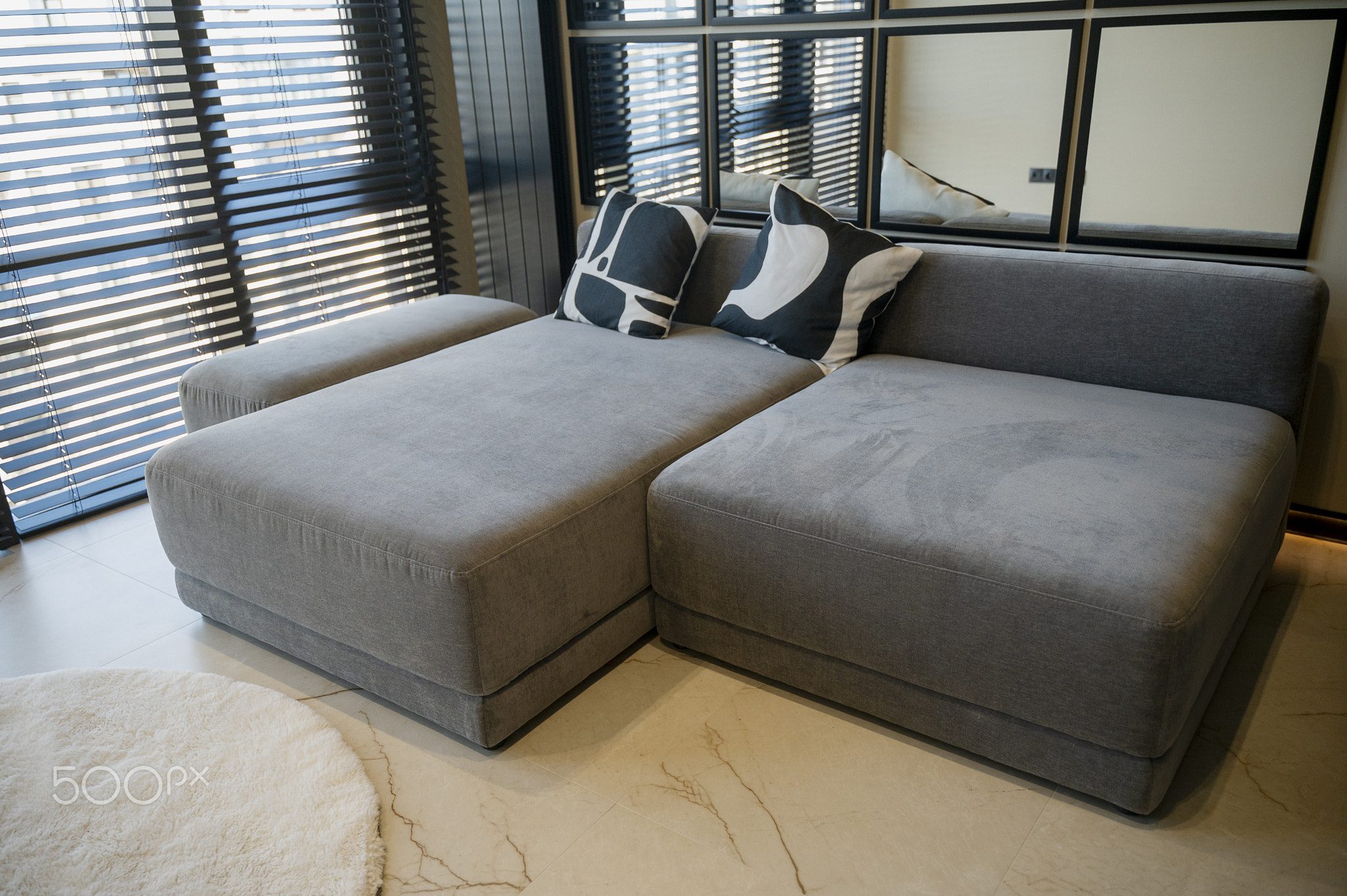 Gray, modern, Ergonomic sofa standing near a large window with blinds and a mirror wal