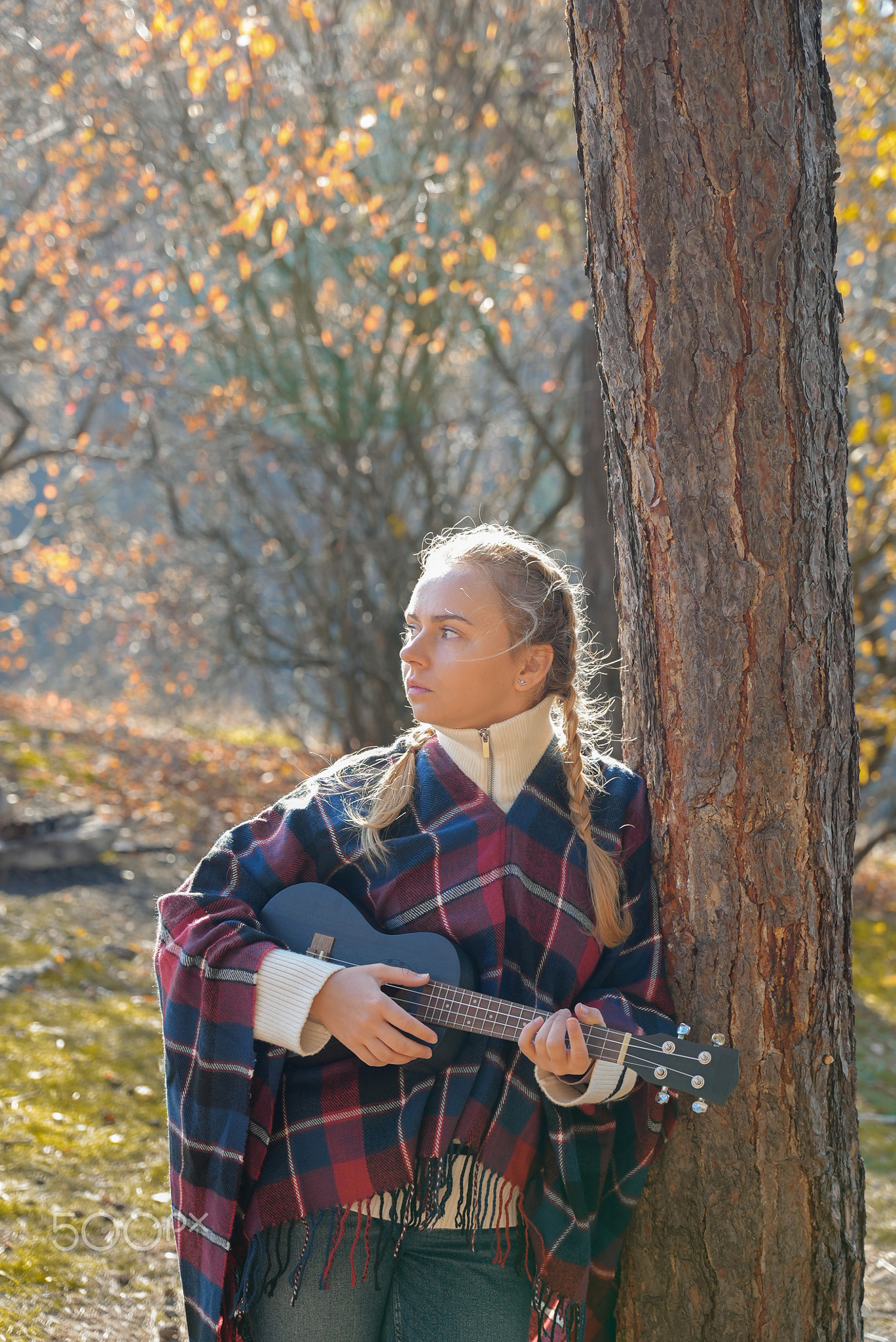 Blonde woman playing guitar ukulele outdoors in autumn forest. Concept