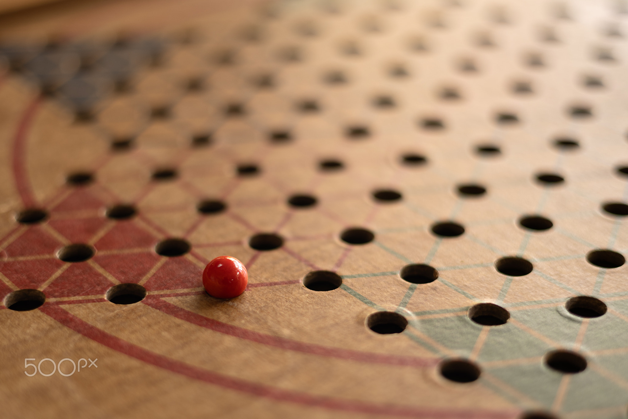 One red marble on a wooden board of Chinese Checkers