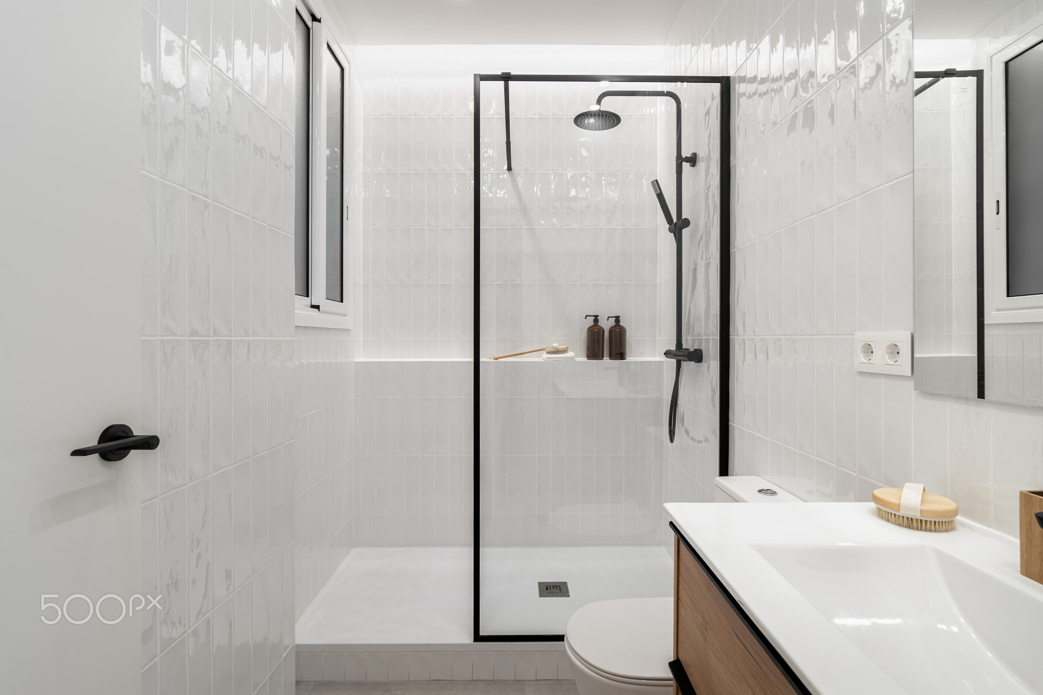 Modern bathroom with a glass shower, white tiles, and wooden accents. Minimalist design featuring a