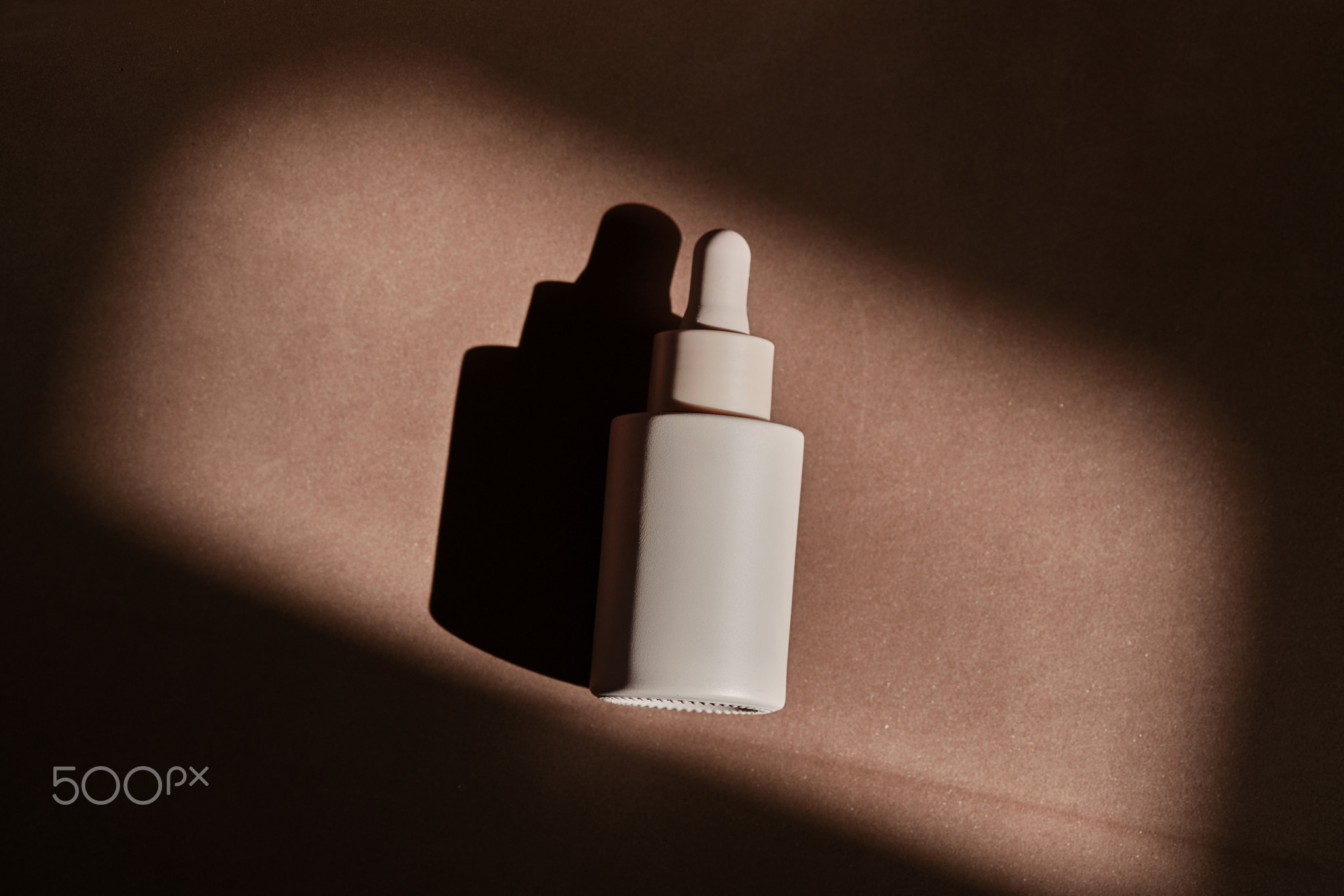 A bottle of face serum on a brown chocolate background.