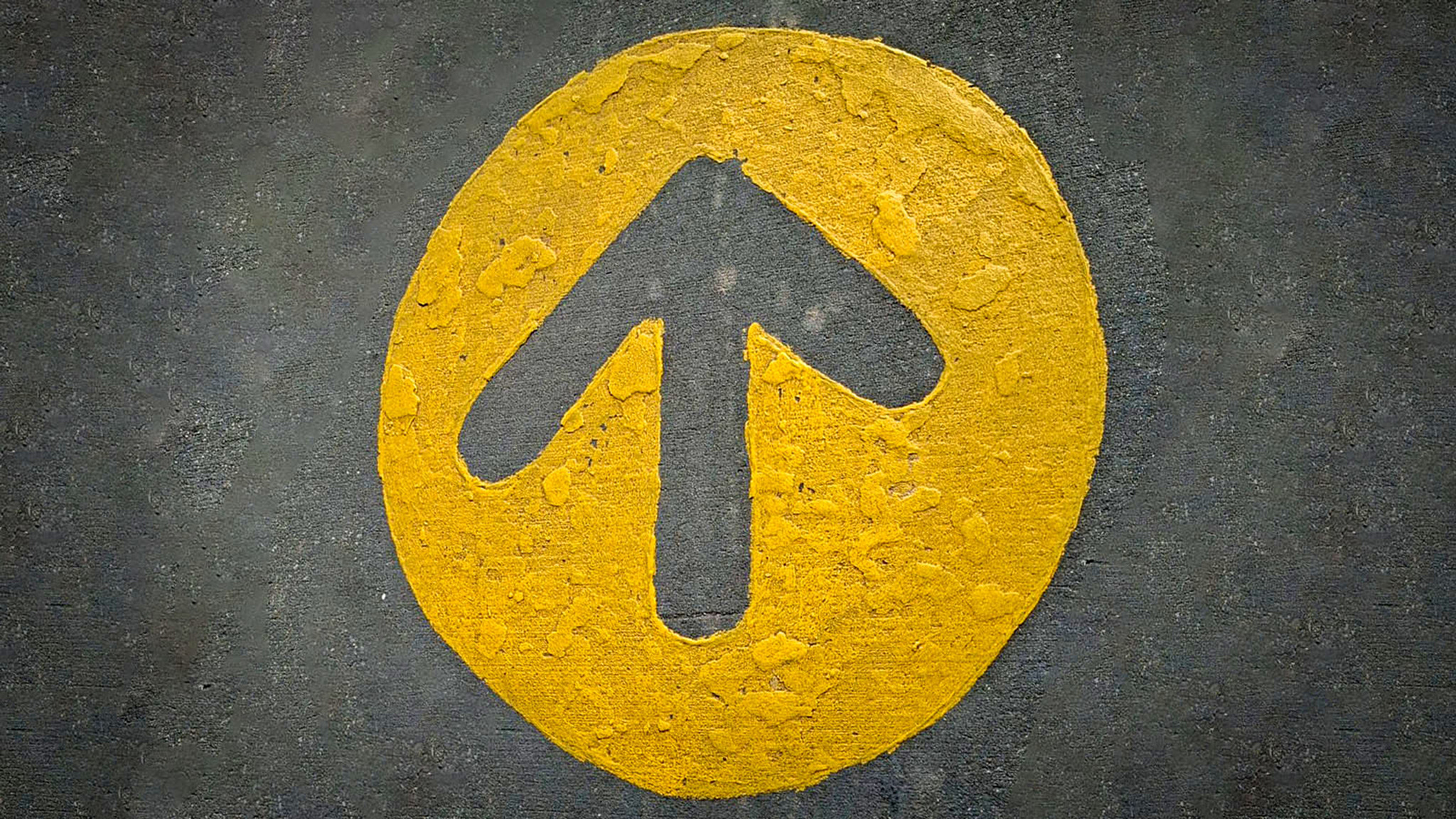 rustic bold yellow arrow points upward inside a circle, stamped on rough dark pavement. Conveys dire