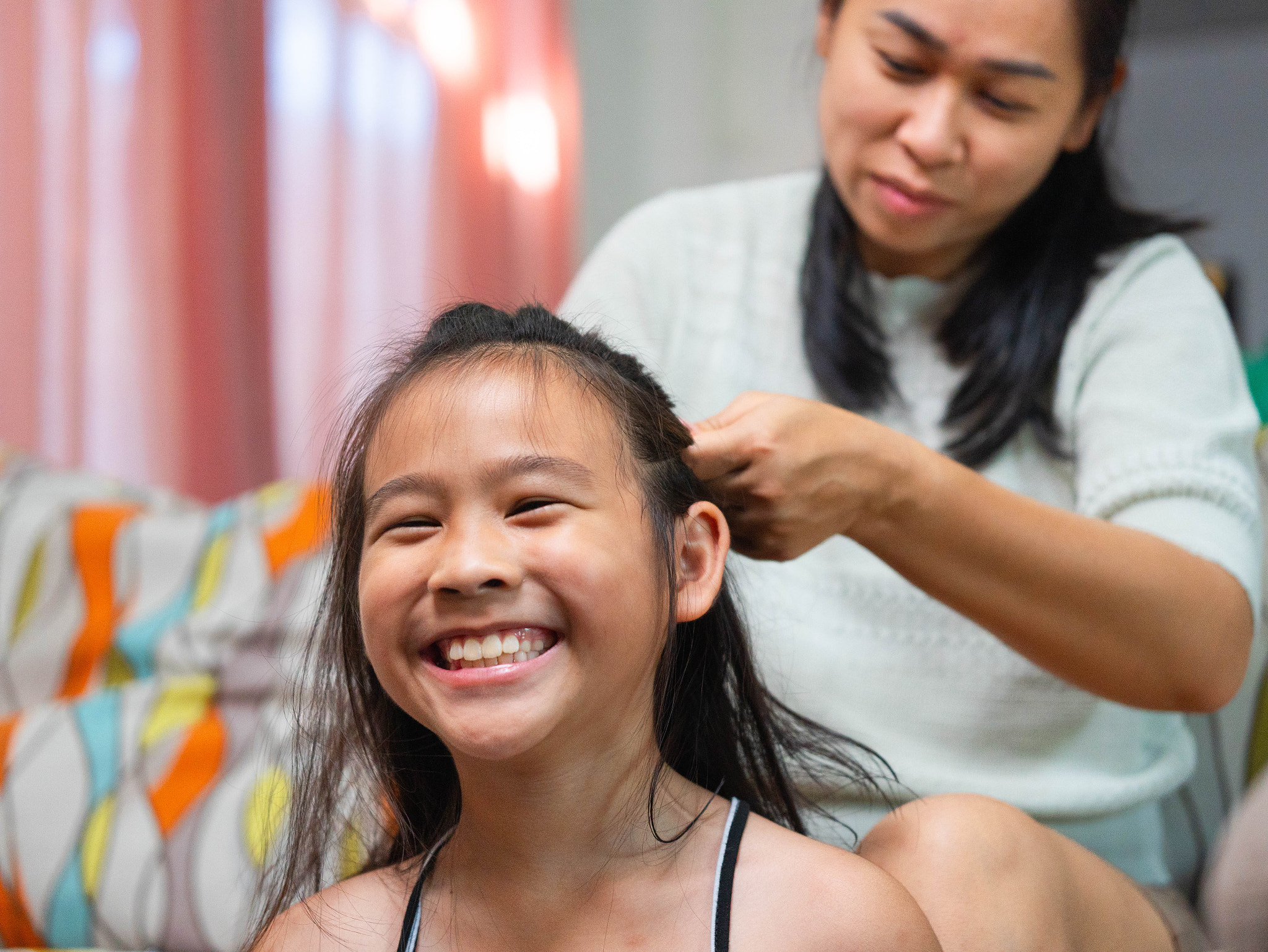 Asian Mother Braiding Daughter's Hair and Sharing a Happy Family Moment at Home.