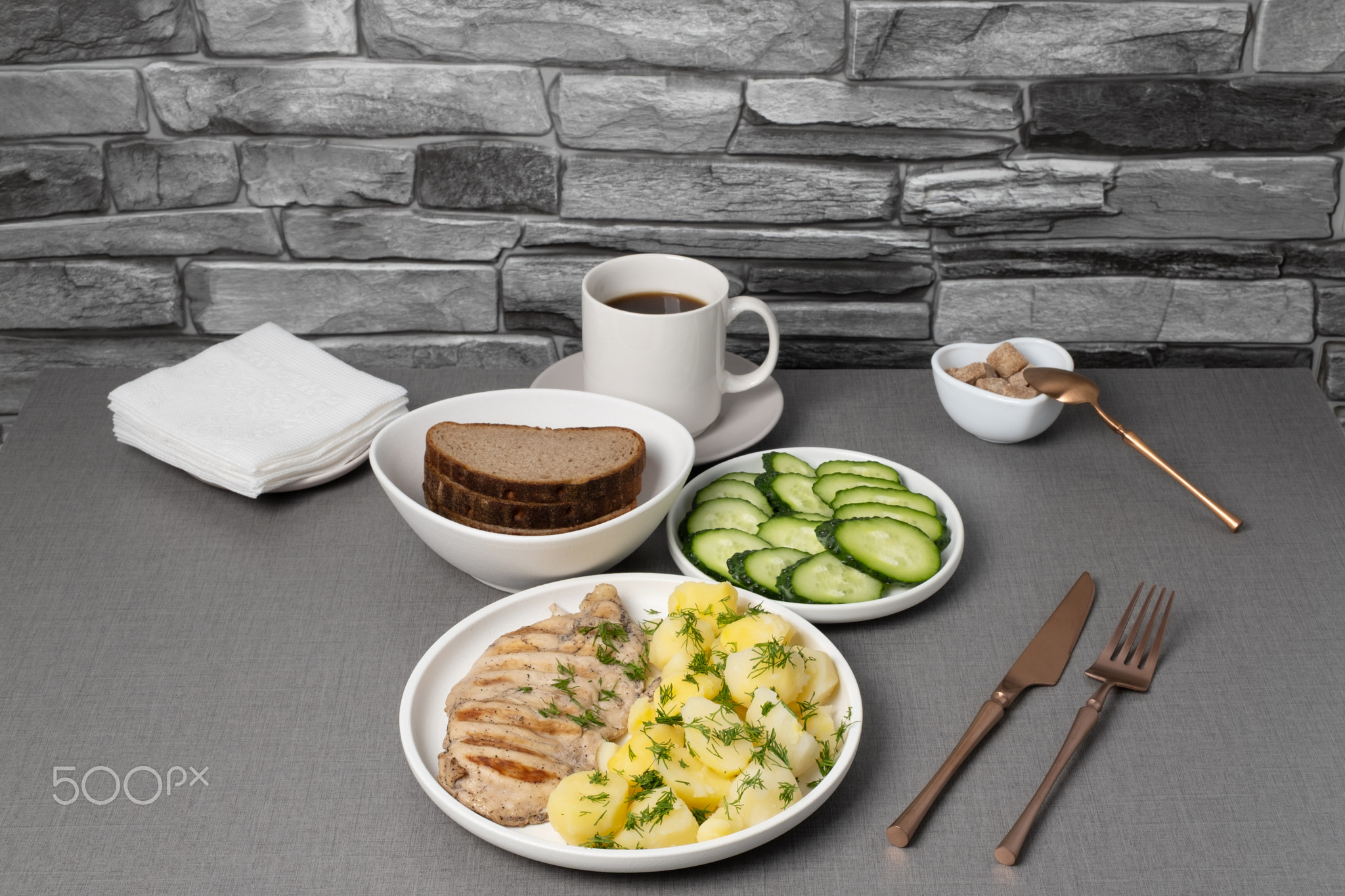 Delicious lunch featuring grilled meat, boiled potatoes, fresh cucumbers, and coffee served