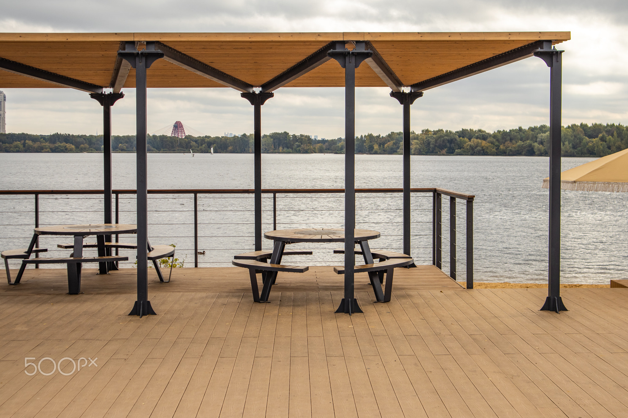 Waterfront terrace with round table under pergola, river view and calm city park