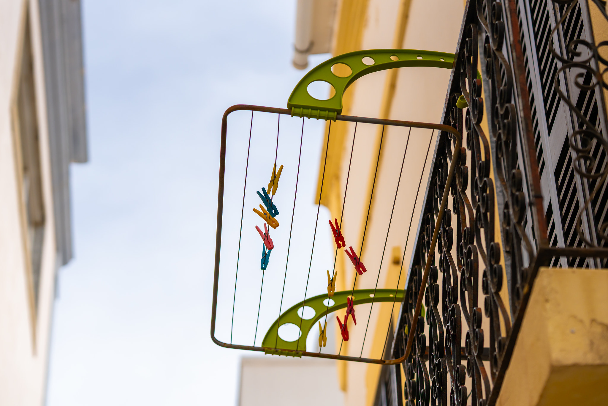 Clothespins in various colors hang from a drying rack attached to a wrought iron balcony railing.