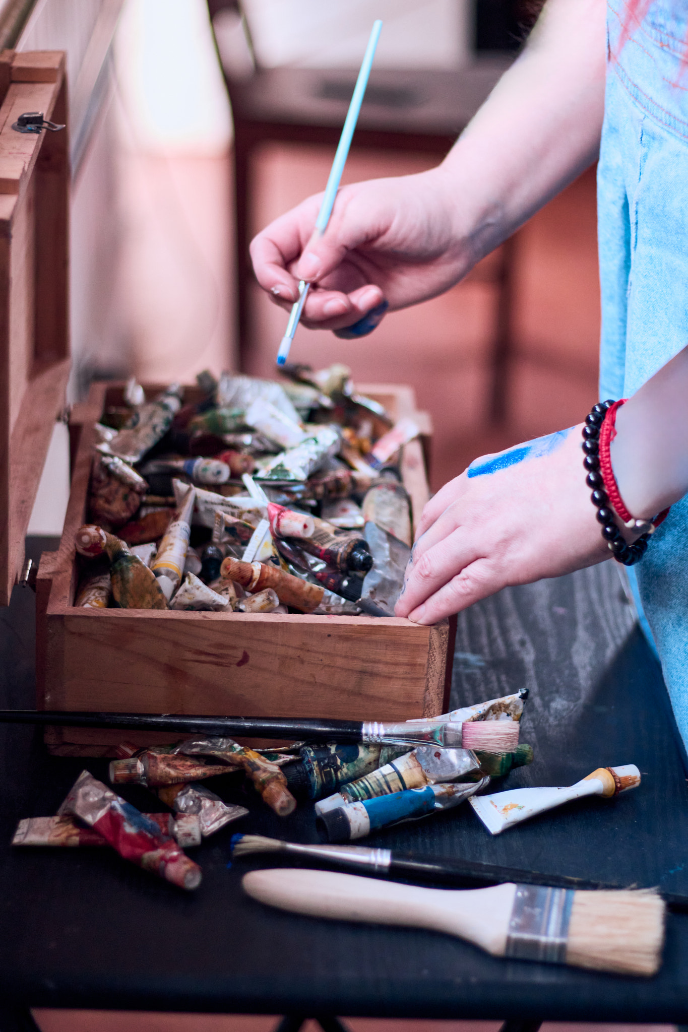 View of a Latina woman's hands next to a box of paints, along with brushes of different shapes