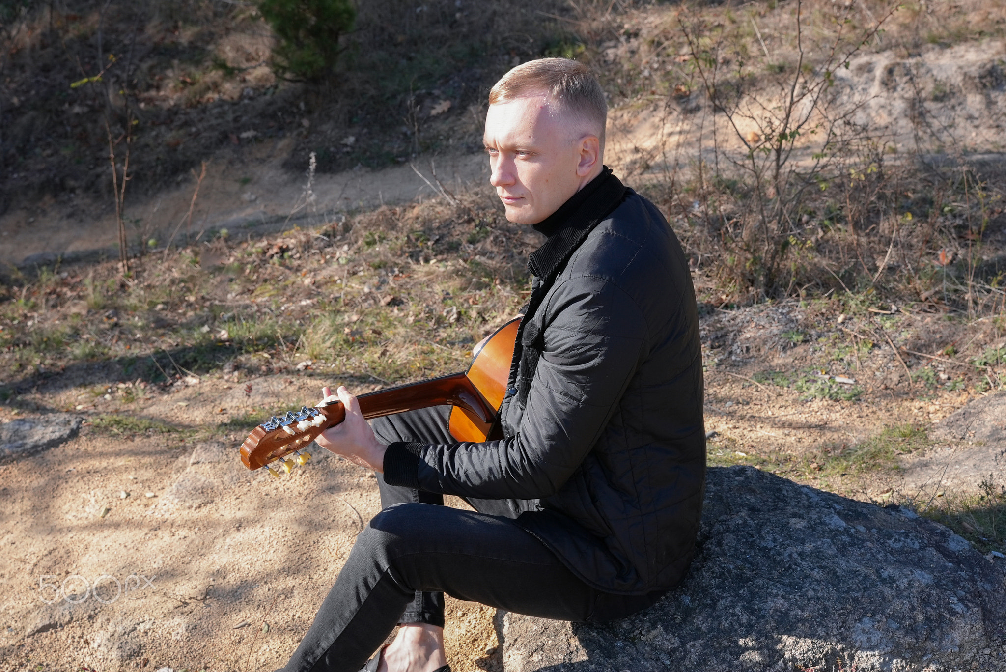 Blonde man playing string guitar outdoors in autumn forest. Concept of