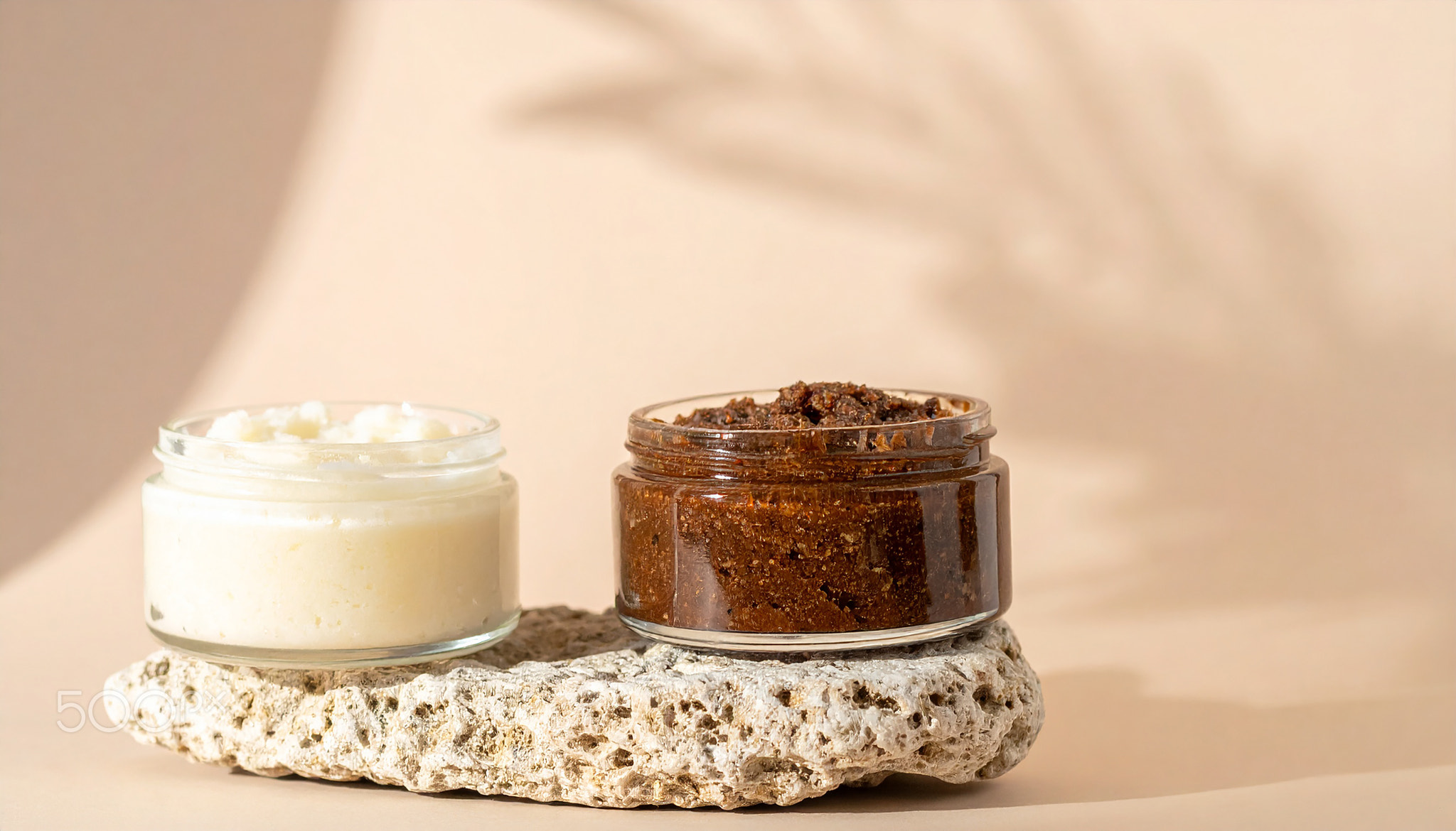 Handcrafted coconut and coffee body scrubs in cream and brown tones in glass jars on stone podium