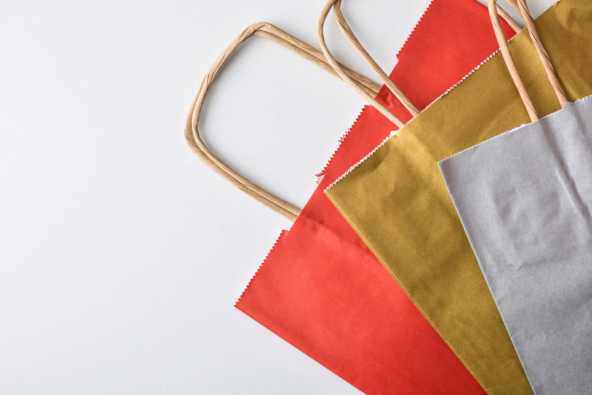 Empty, folded red, gold, and silver paper shopping bags