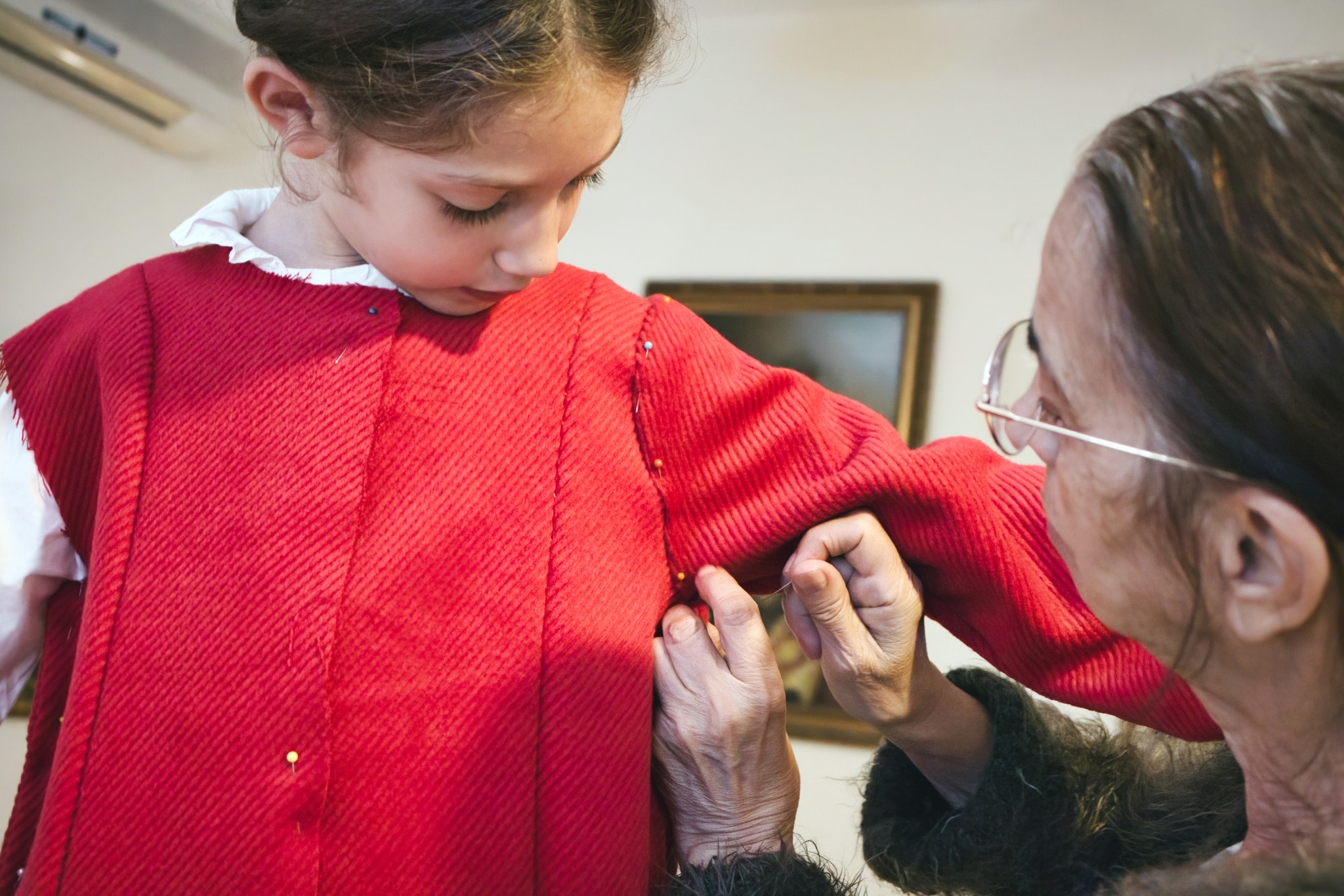 A cute little white Caucasian girl being fitted for a made-to-measure red dress by a seamstress