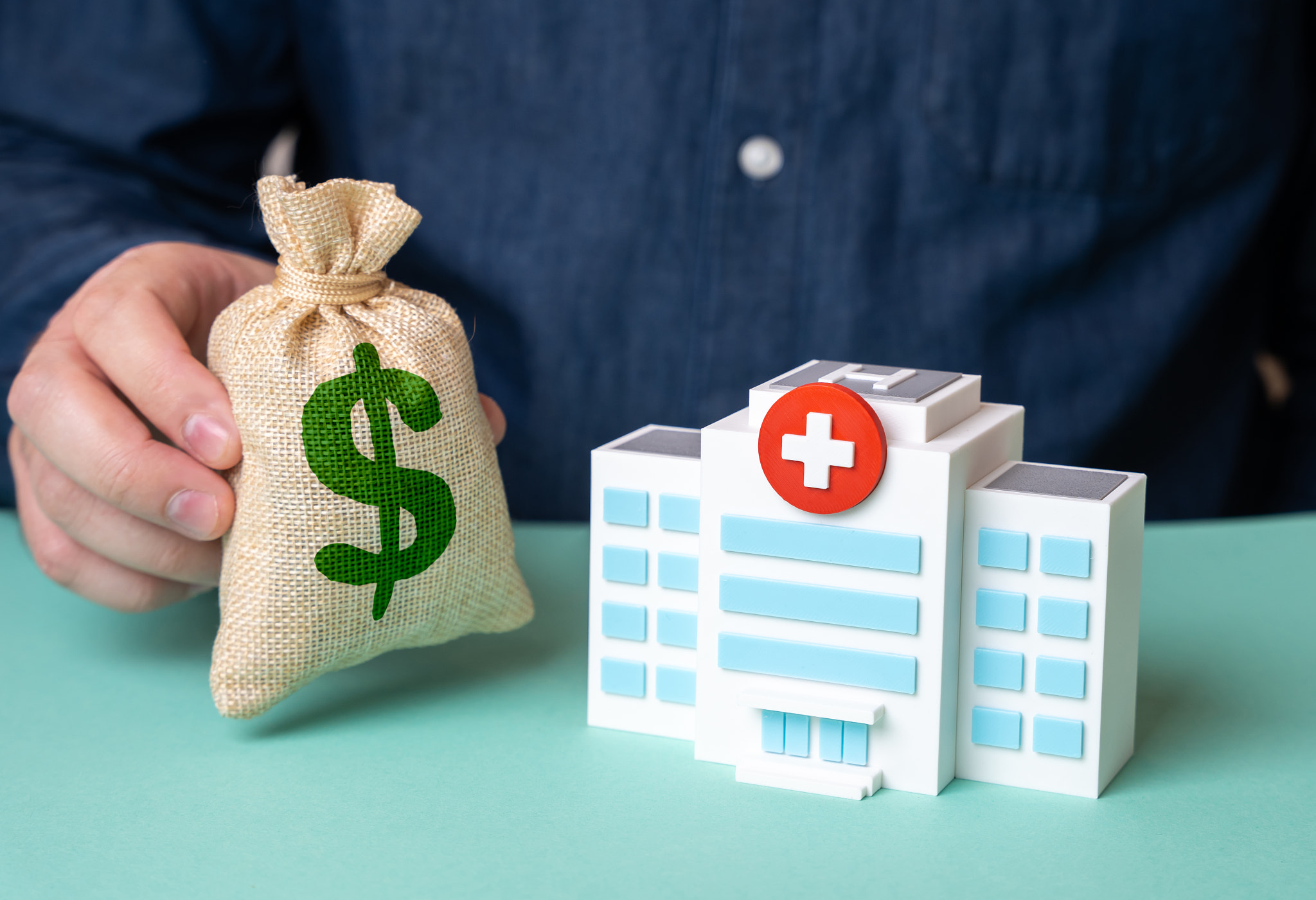 Man holding dollar money bag near hospital building. Investments in medicine, charity fund. Healthca