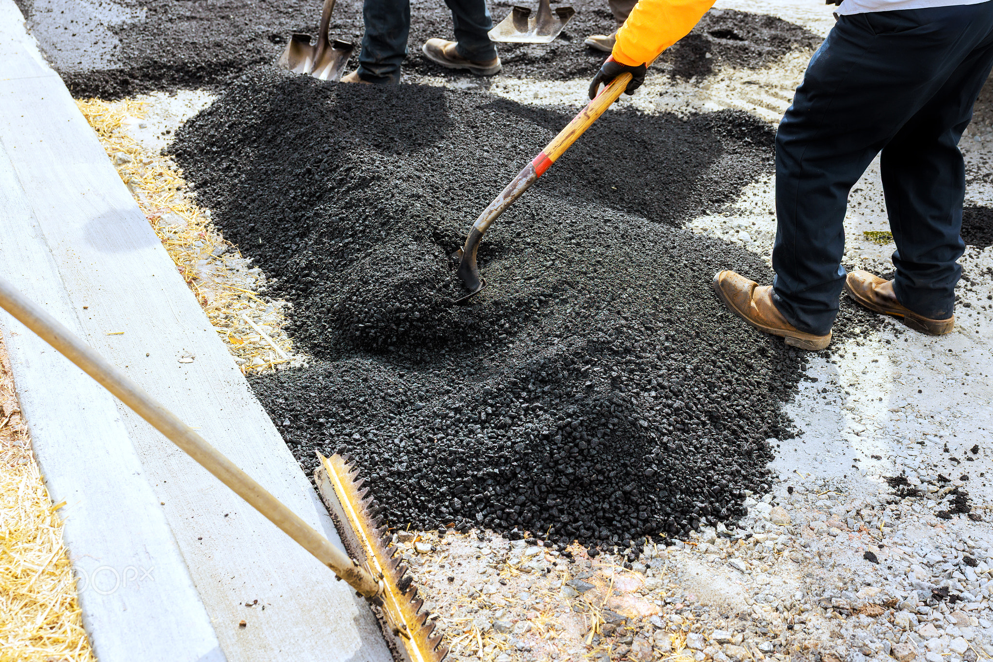 Workers laying asphalt for road construction with shovels on suburban