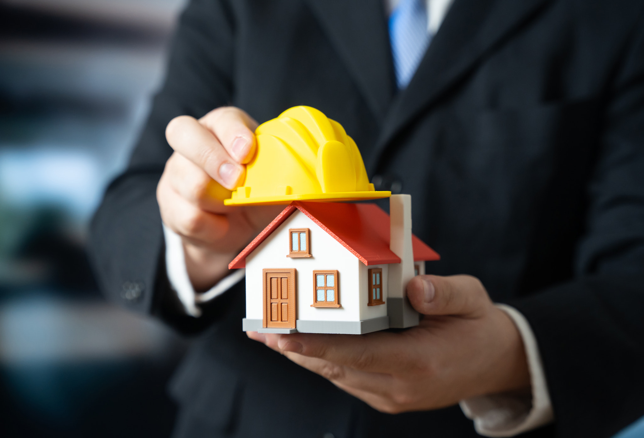 A man puts a yellow construction helmet on a house. House renovation. Building reconstruction. Struc