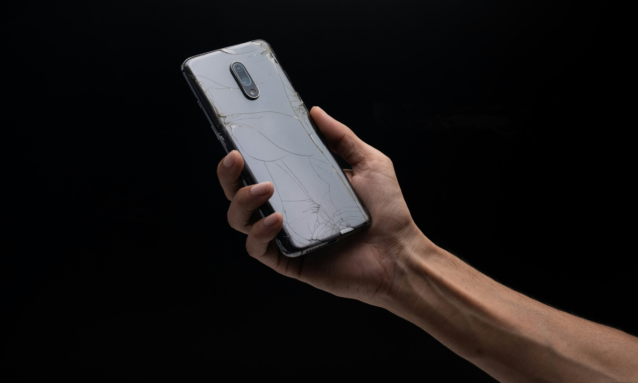 Hand Holding a Cracked Smartphone Against Dark Background