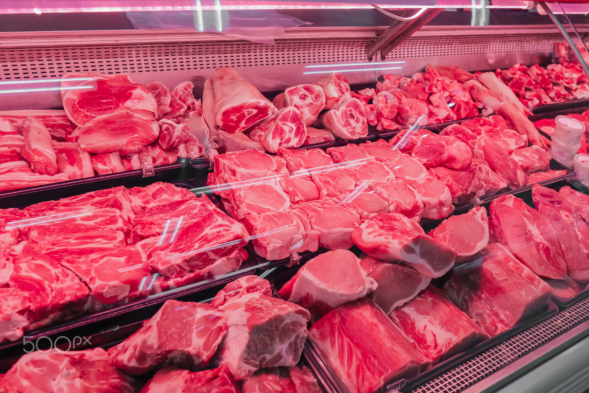 Chilled fresh meat, beef or pork fillet on a display case with red lighting. Meat merchandising at a