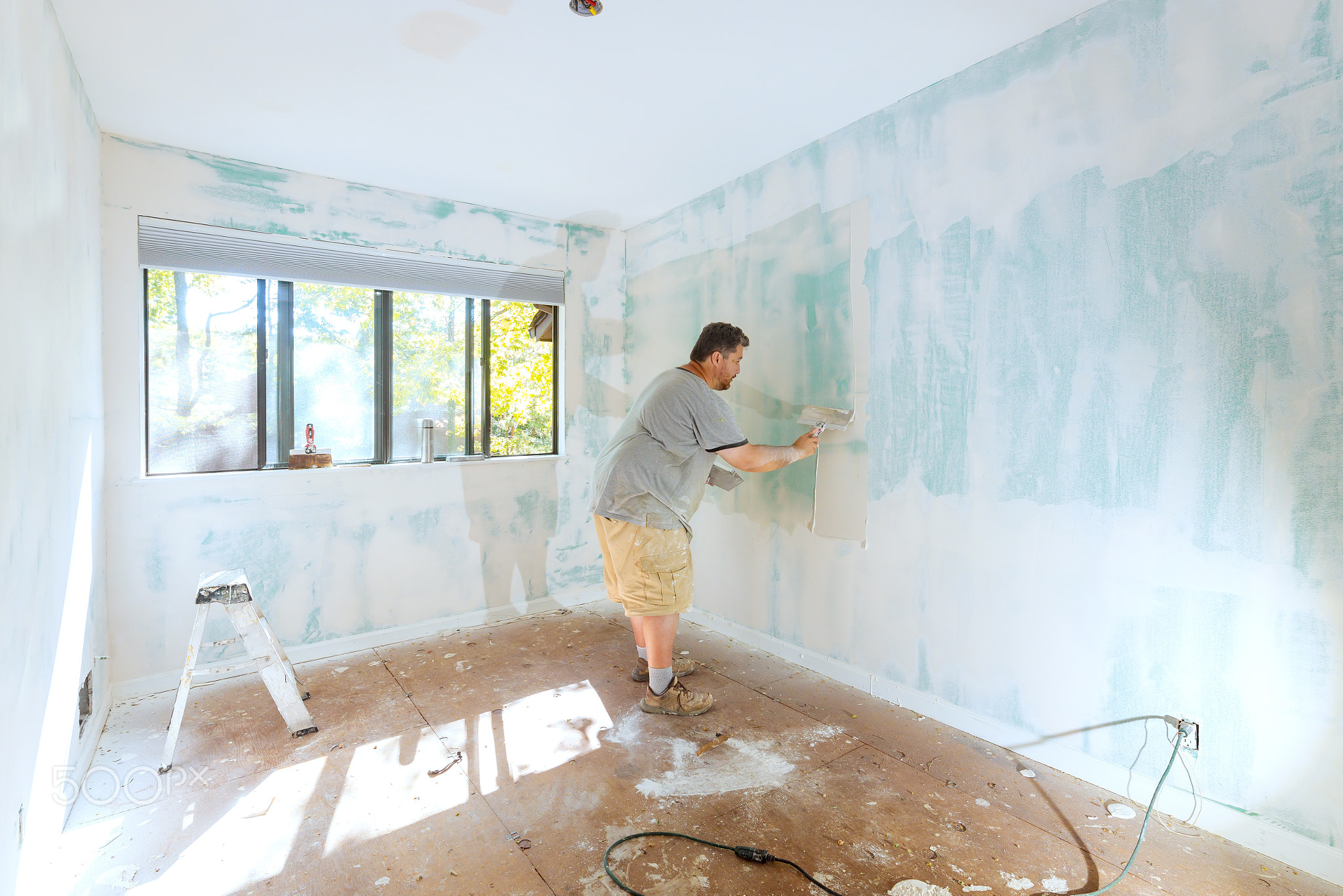 Person applies putty to a wall in an empty room during daylight, with
