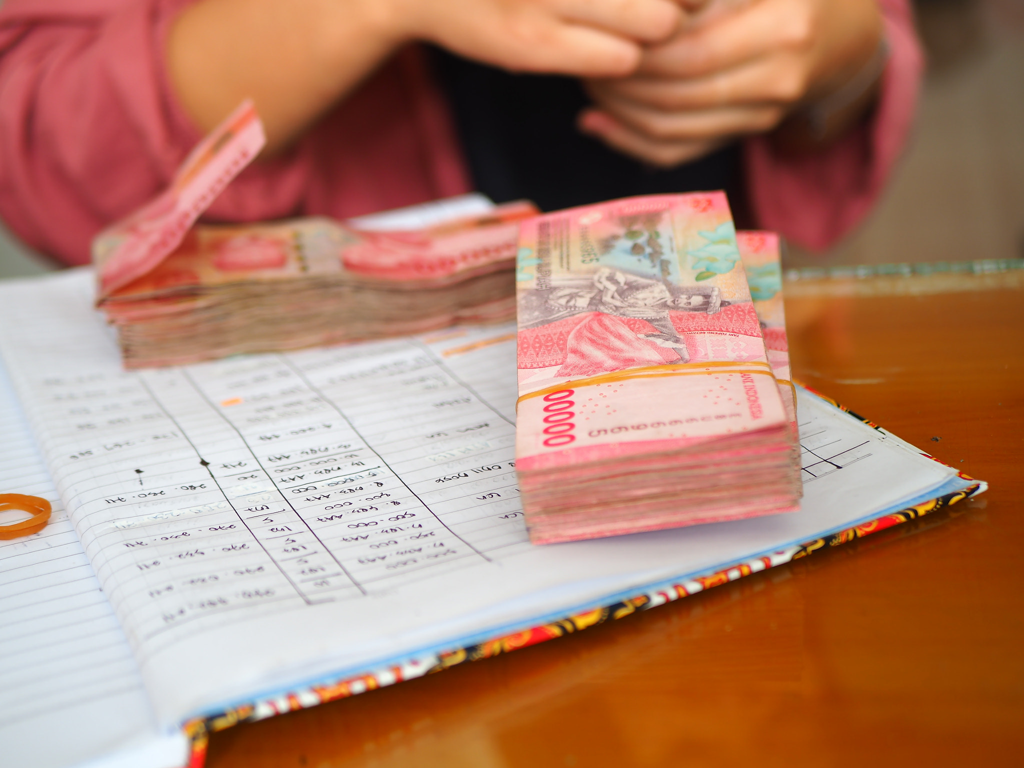 Stack of Indonesian Rupiah notes sits atop an open ledger being counted by someone in the background