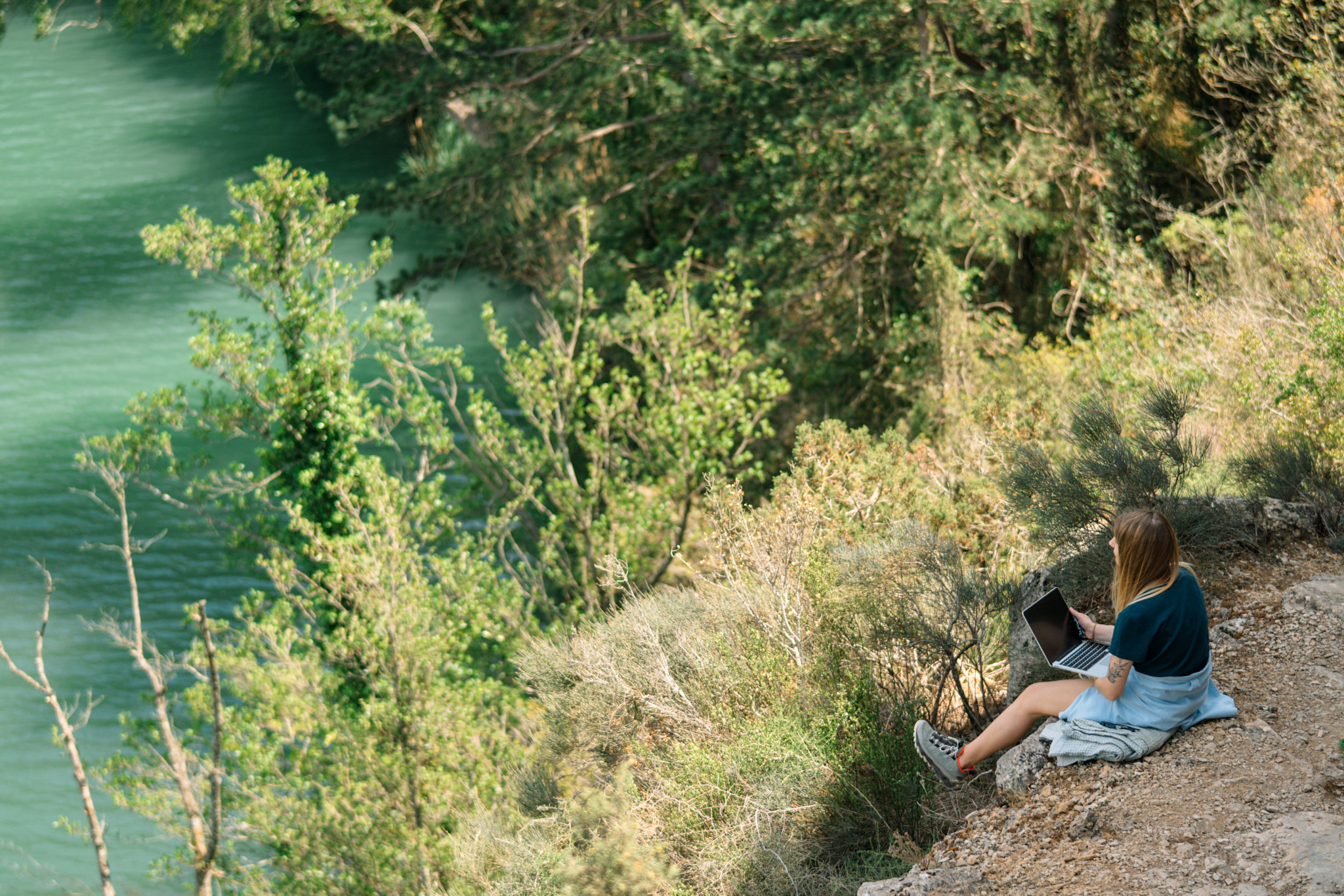 Woman with laptop while sitting on rock by lake