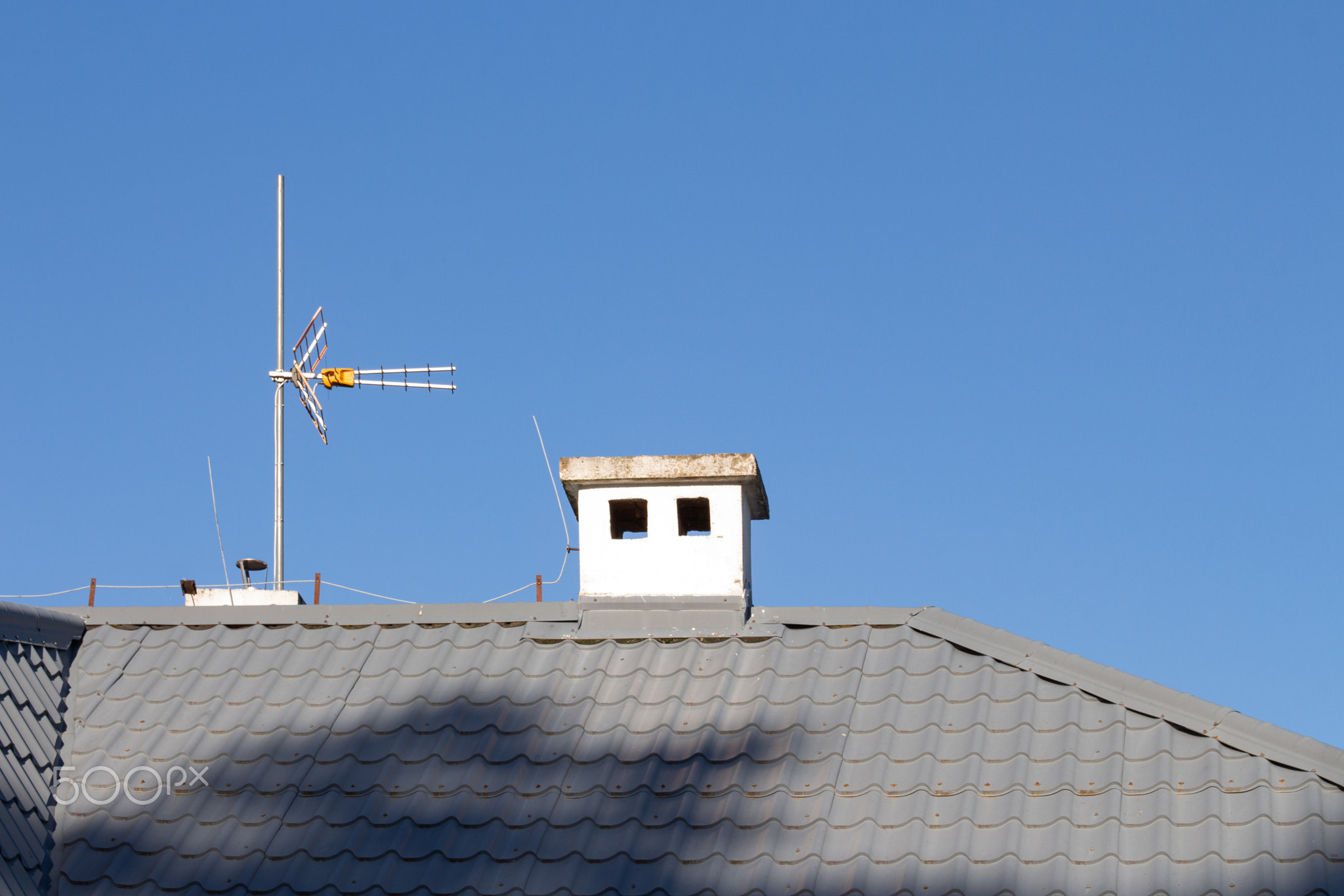 Chimney and antenna on a sloped roof under a clear blue sky at midday