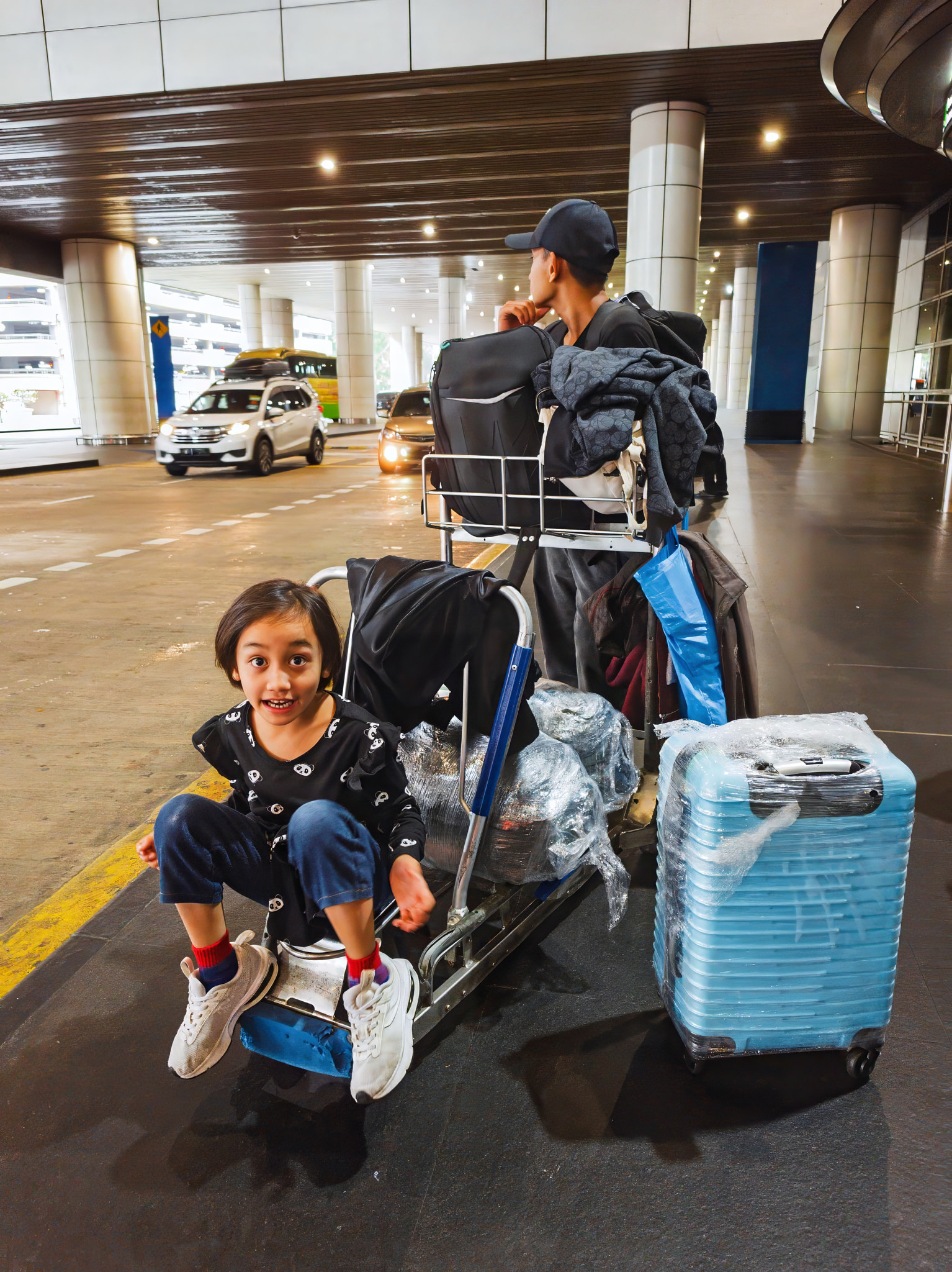 A little girl with her older brother waiting for car with trolley at the airport in Malaysia.