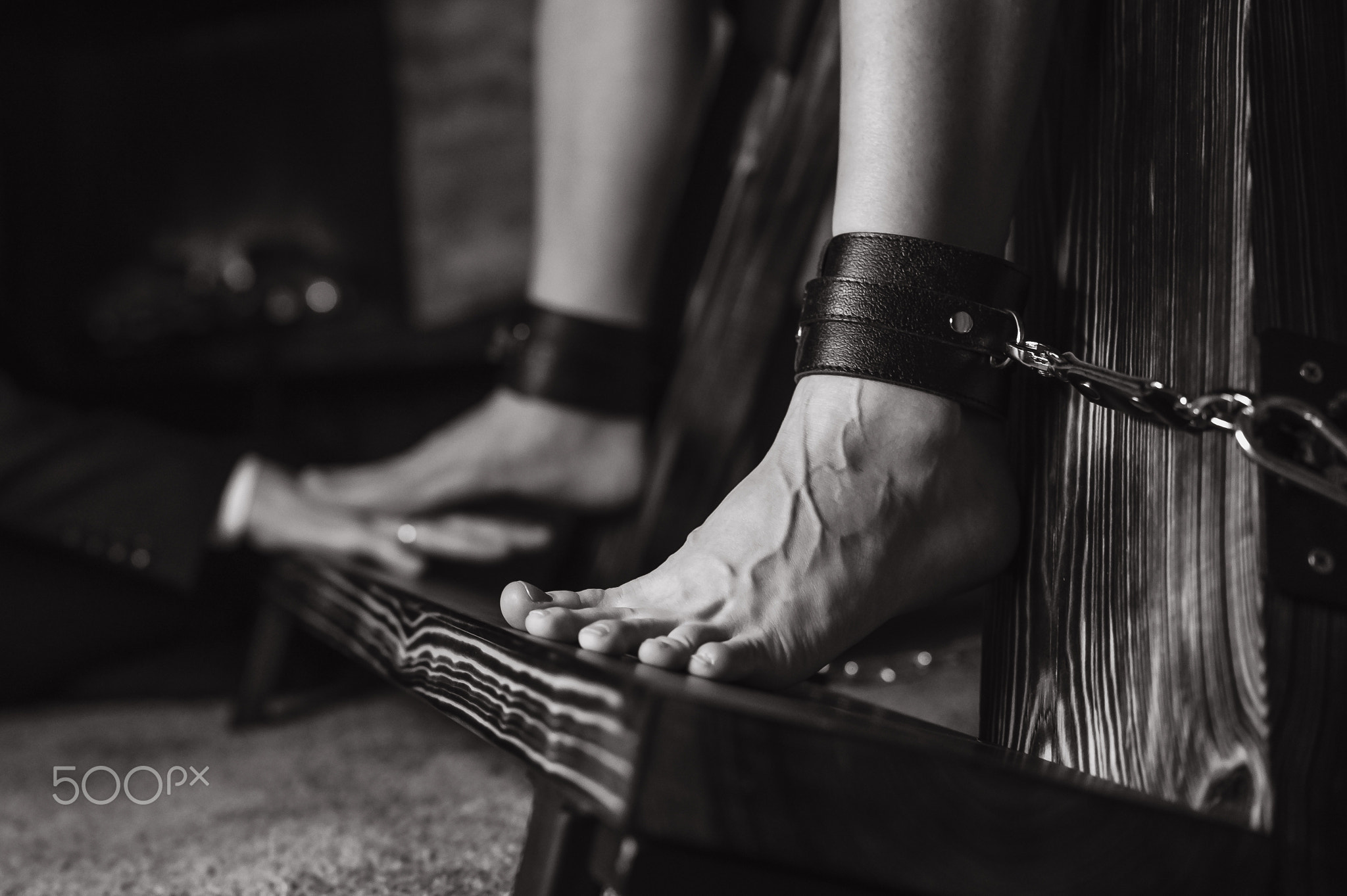 A man chains a woman's legs to a BDSM cross.