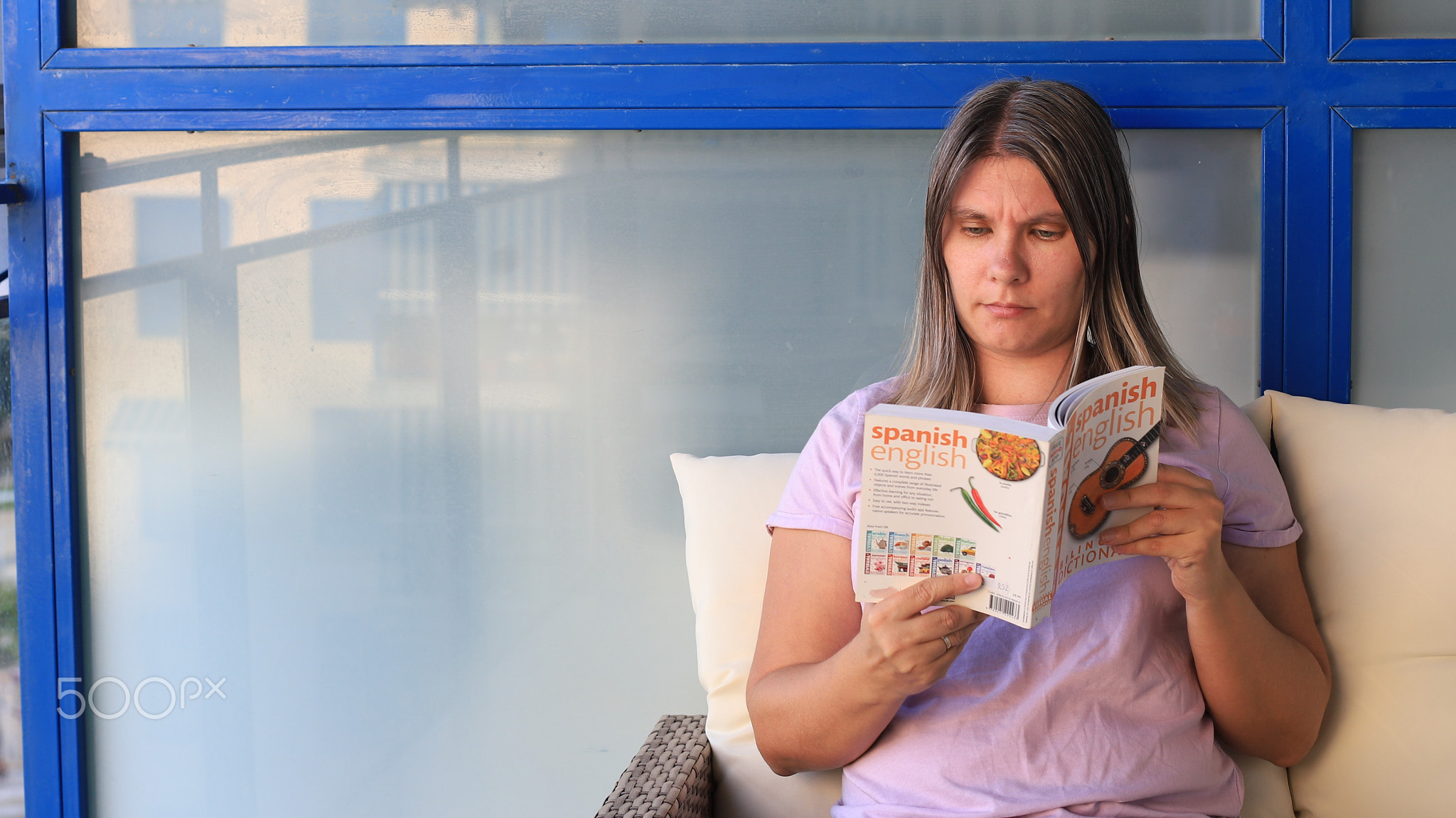 Woman reading a bilingual Spanish-English language book while seated on a chair 
