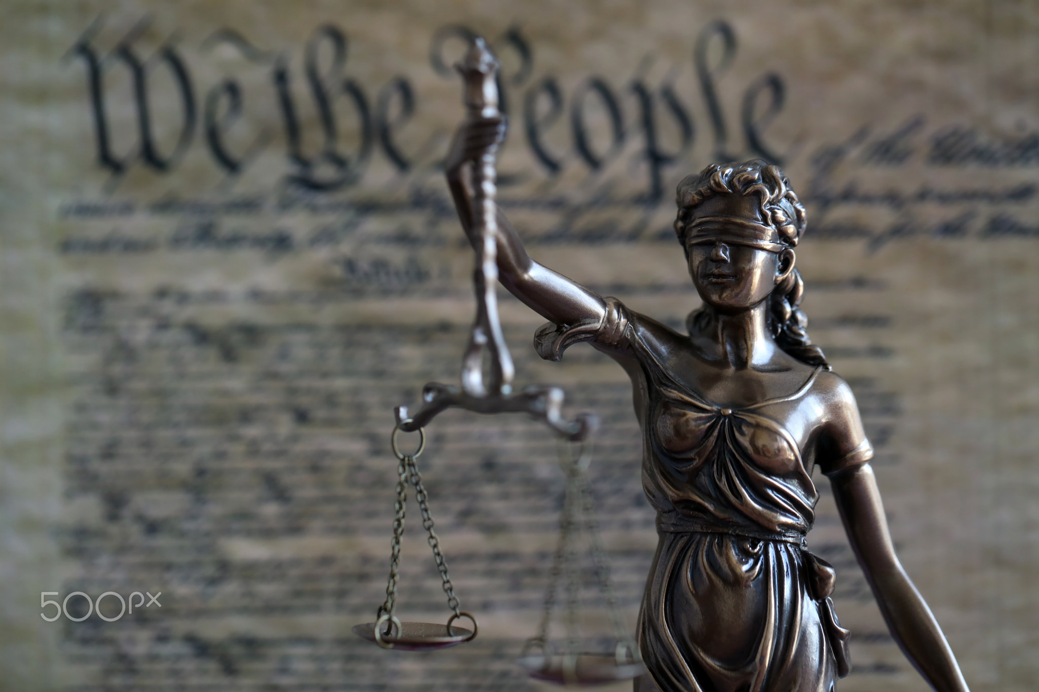 Dark scene with Lady Justice and background of blurred US Constitution page
