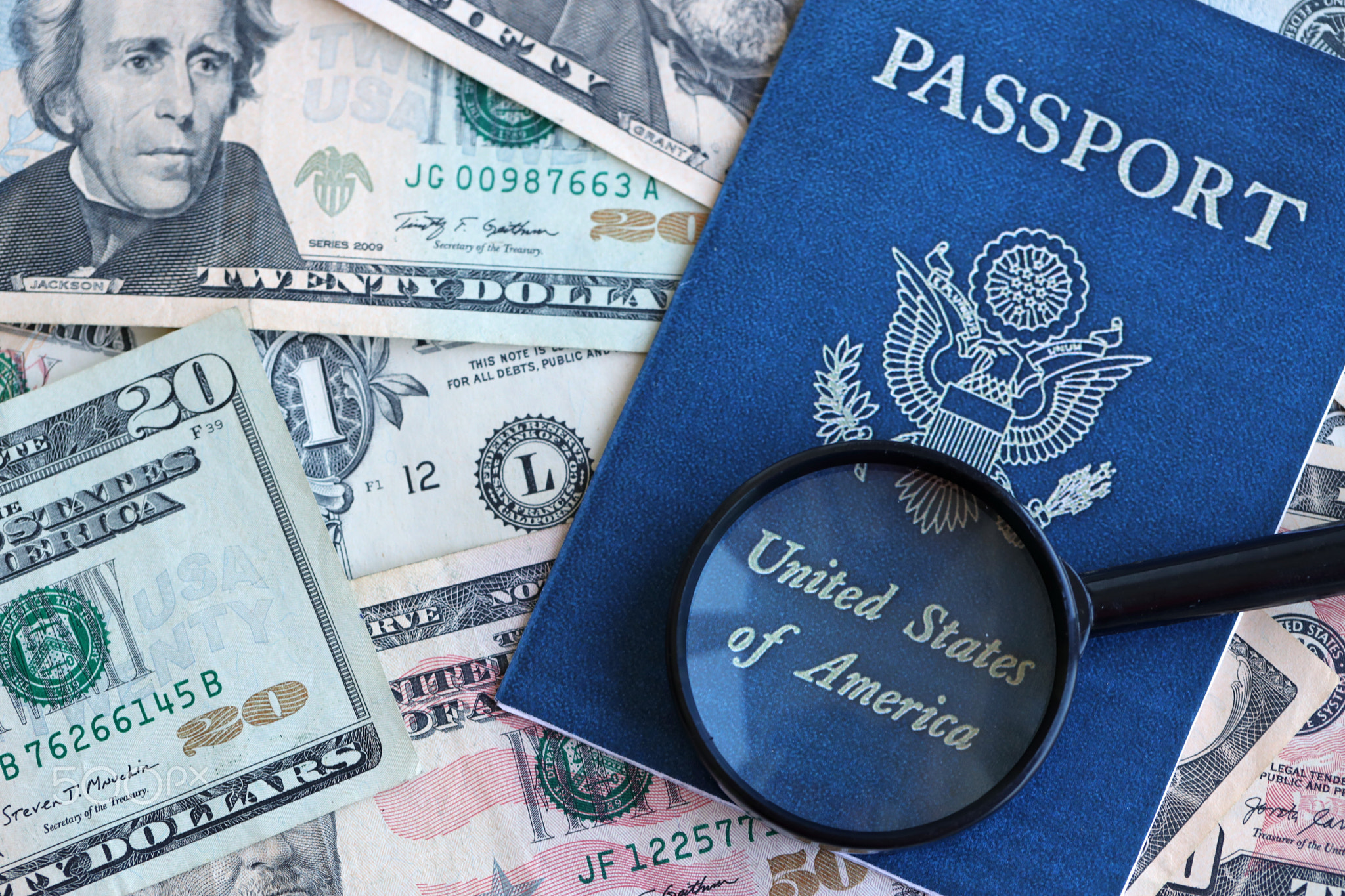 US passport and magnifying glass on the background of many dollar bills