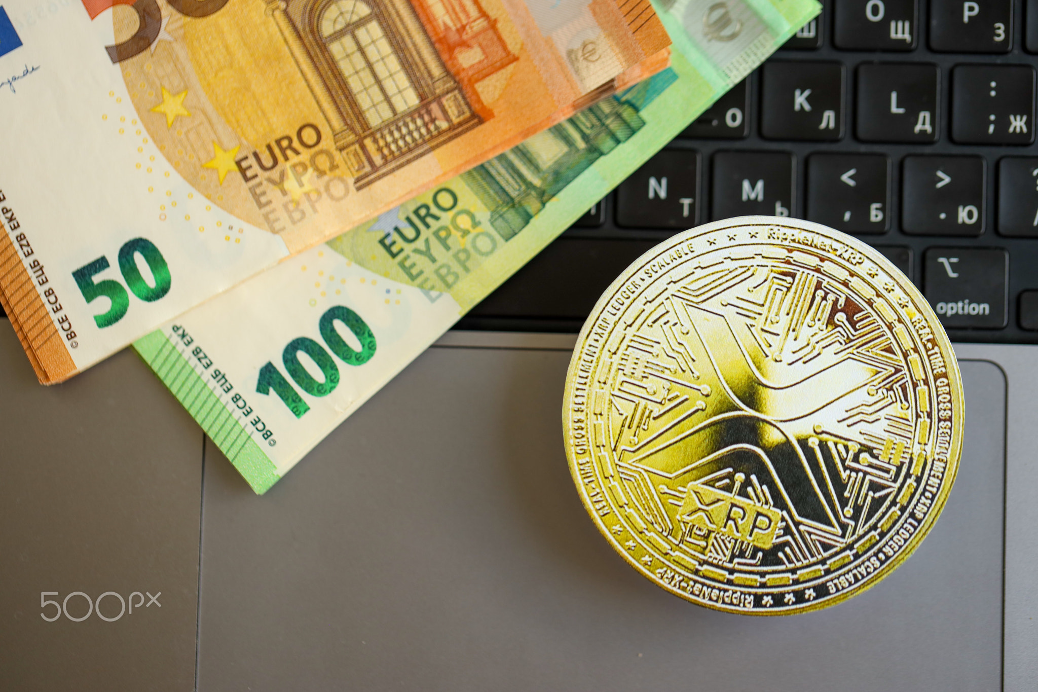 Ripple XRP Coin with big amount of european euro bills on laptop surface