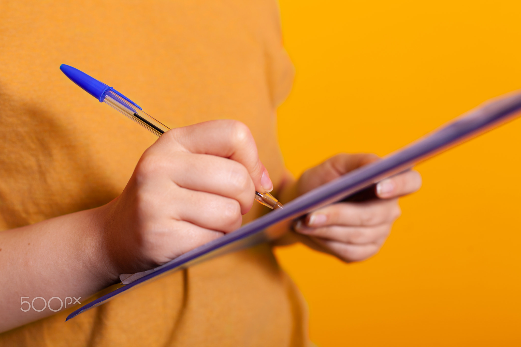Close up of hand holding pen and writing on clipboard papers